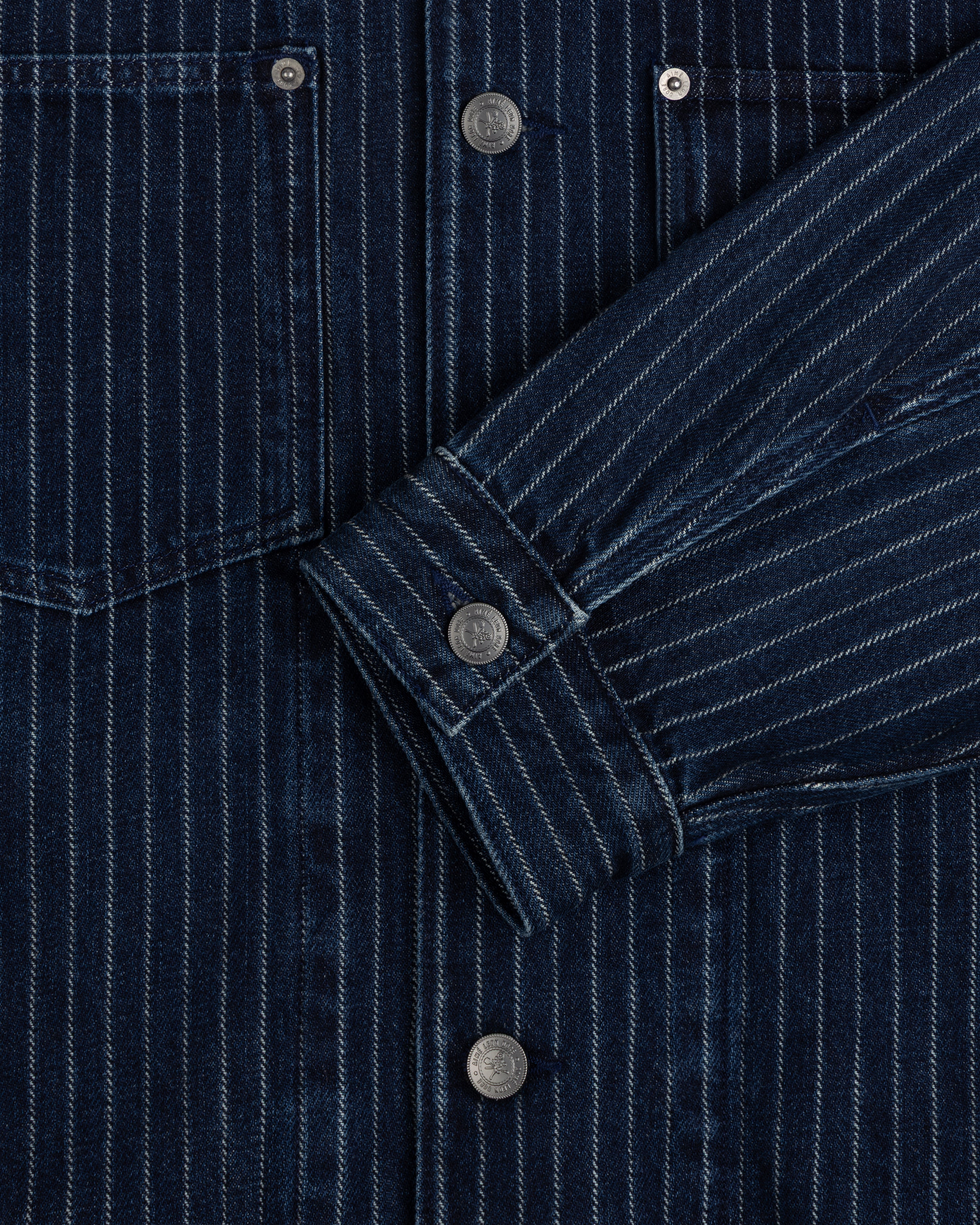 Close-up of the Chalk Stripe Denim Trucker Jacket featuring dark blue pinstripes, metal buttons, and a front pocket.