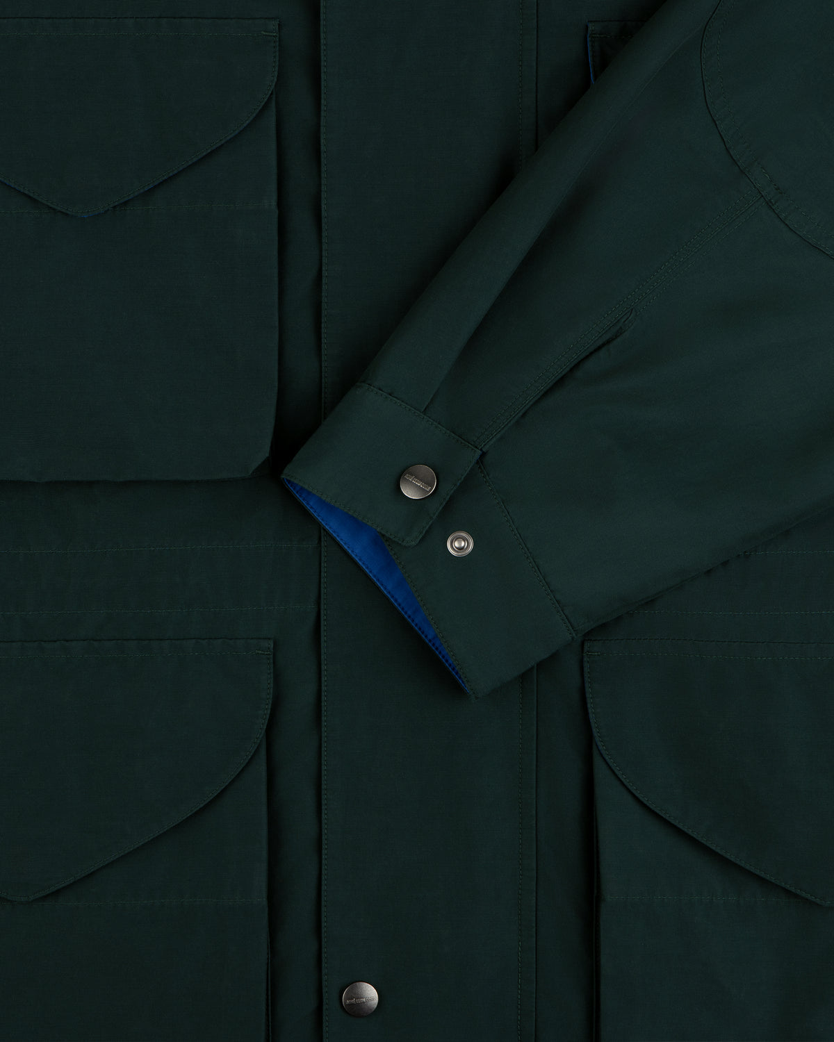 Lightweight Barn Jacket in dark green with flap pockets and snap buttons, shown with sleeve crossed at the front.