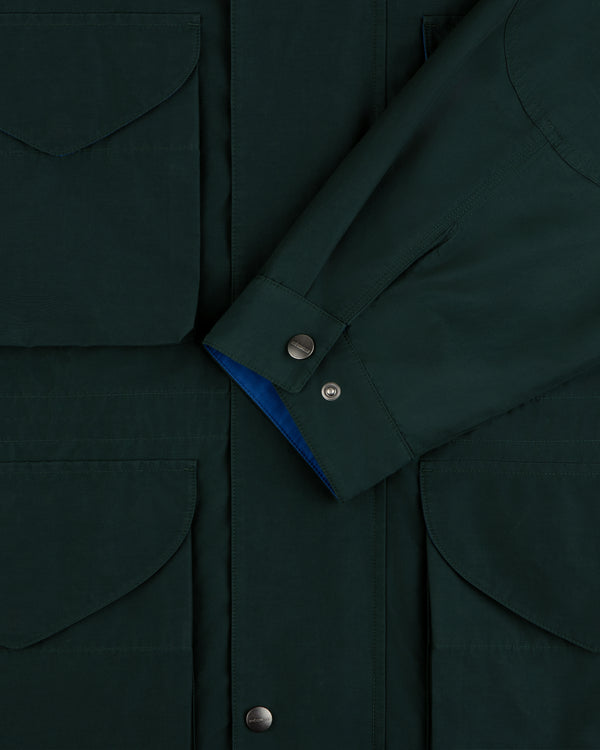 Lightweight Barn Jacket in dark green with flap pockets and snap buttons, shown with sleeve crossed at the front.