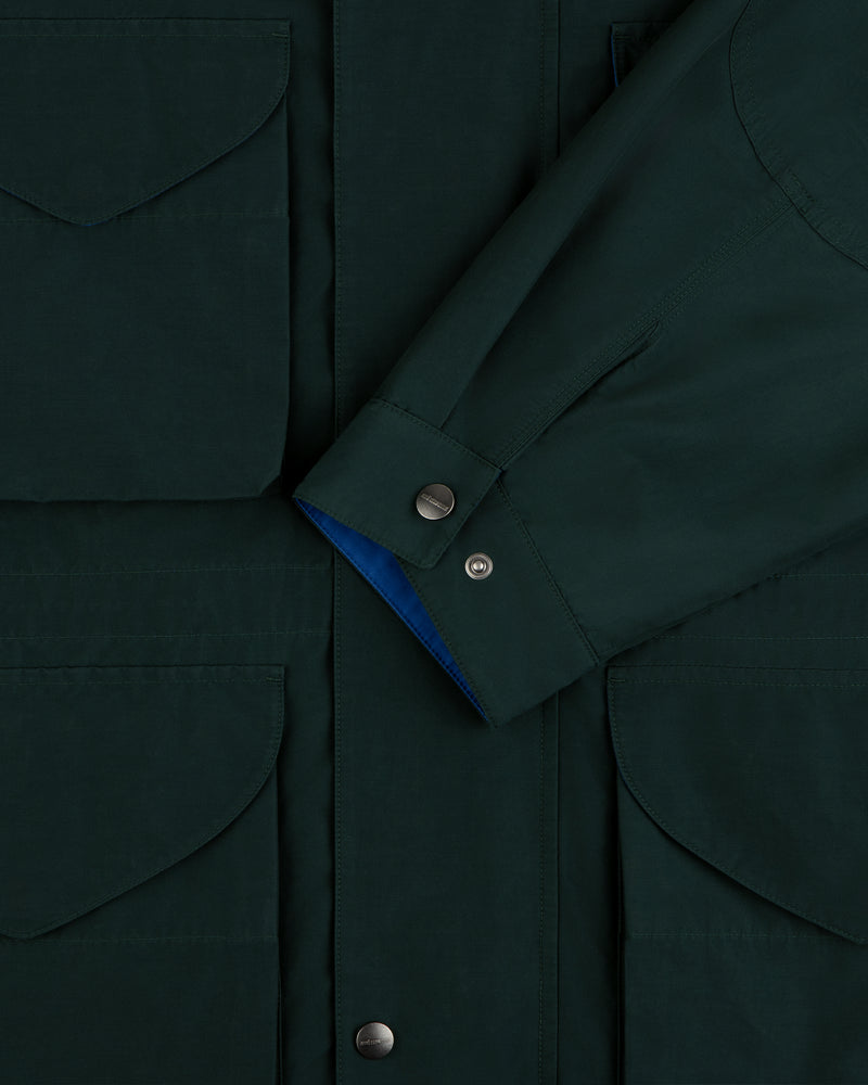 Lightweight Barn Jacket in dark green with flap pockets and snap buttons, shown with sleeve crossed at the front.