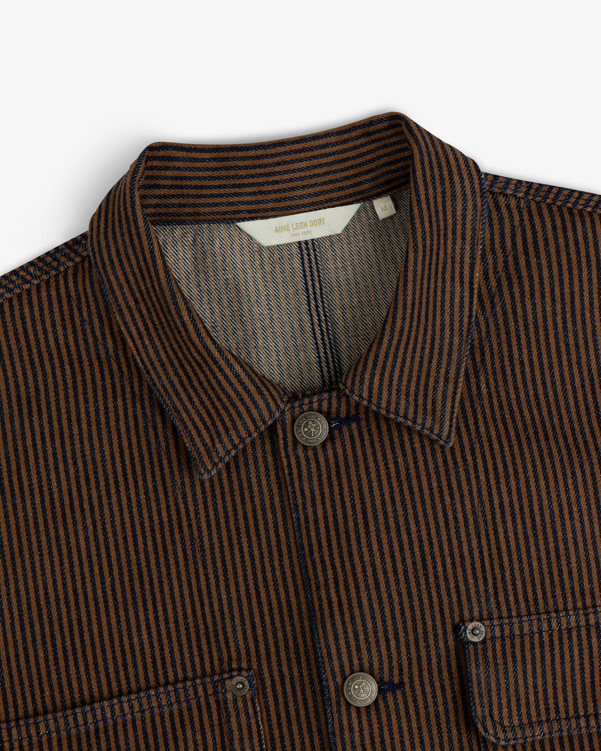 Hickory Stripe Denim Trucker Jacket with collar, chest pockets, and button closures in brown and navy stripes, top view.