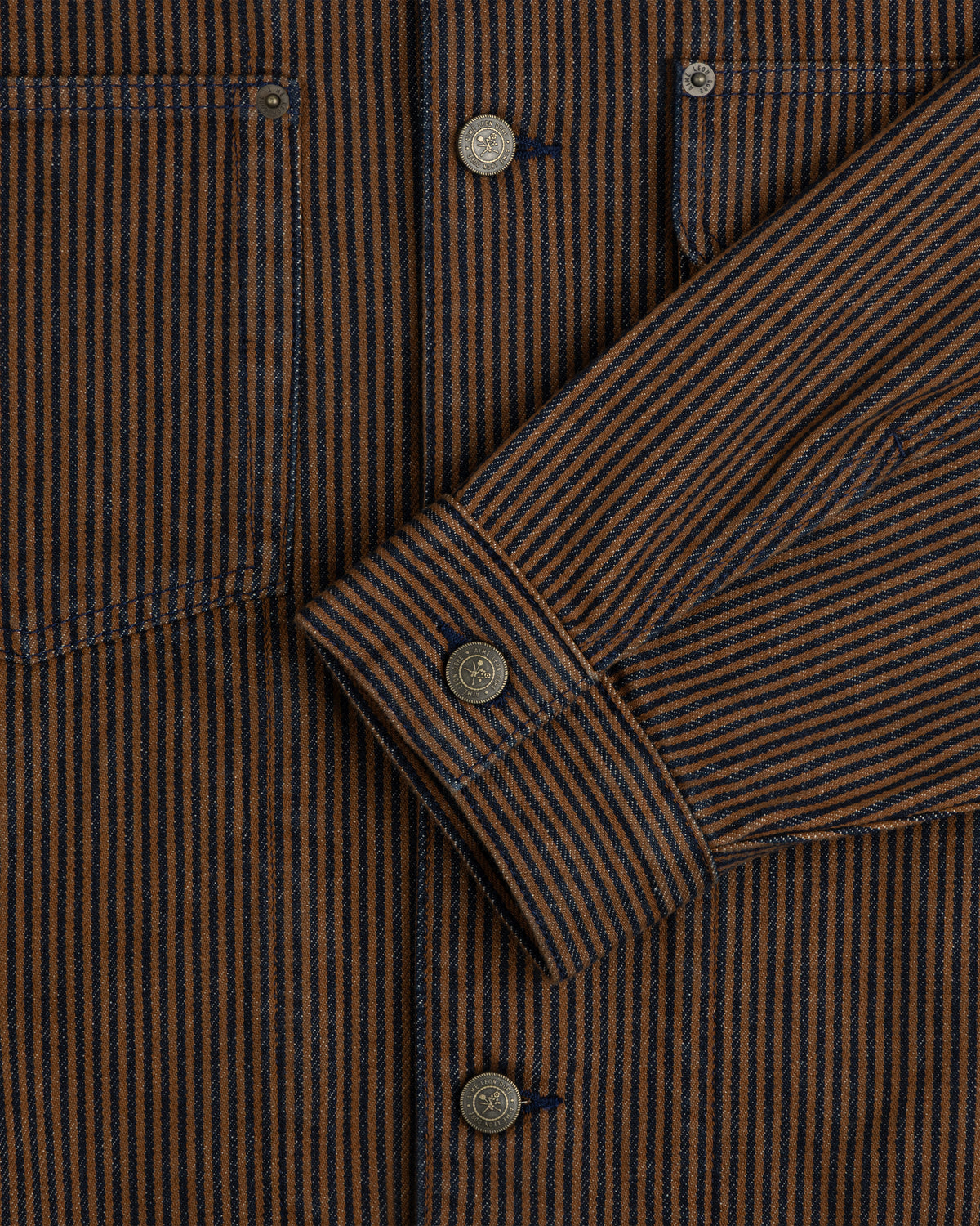 Close-up of the Hickory Stripe Denim Trucker Jacket with brown/navy stripes, metal buttons, and detailed pockets/sleeves.