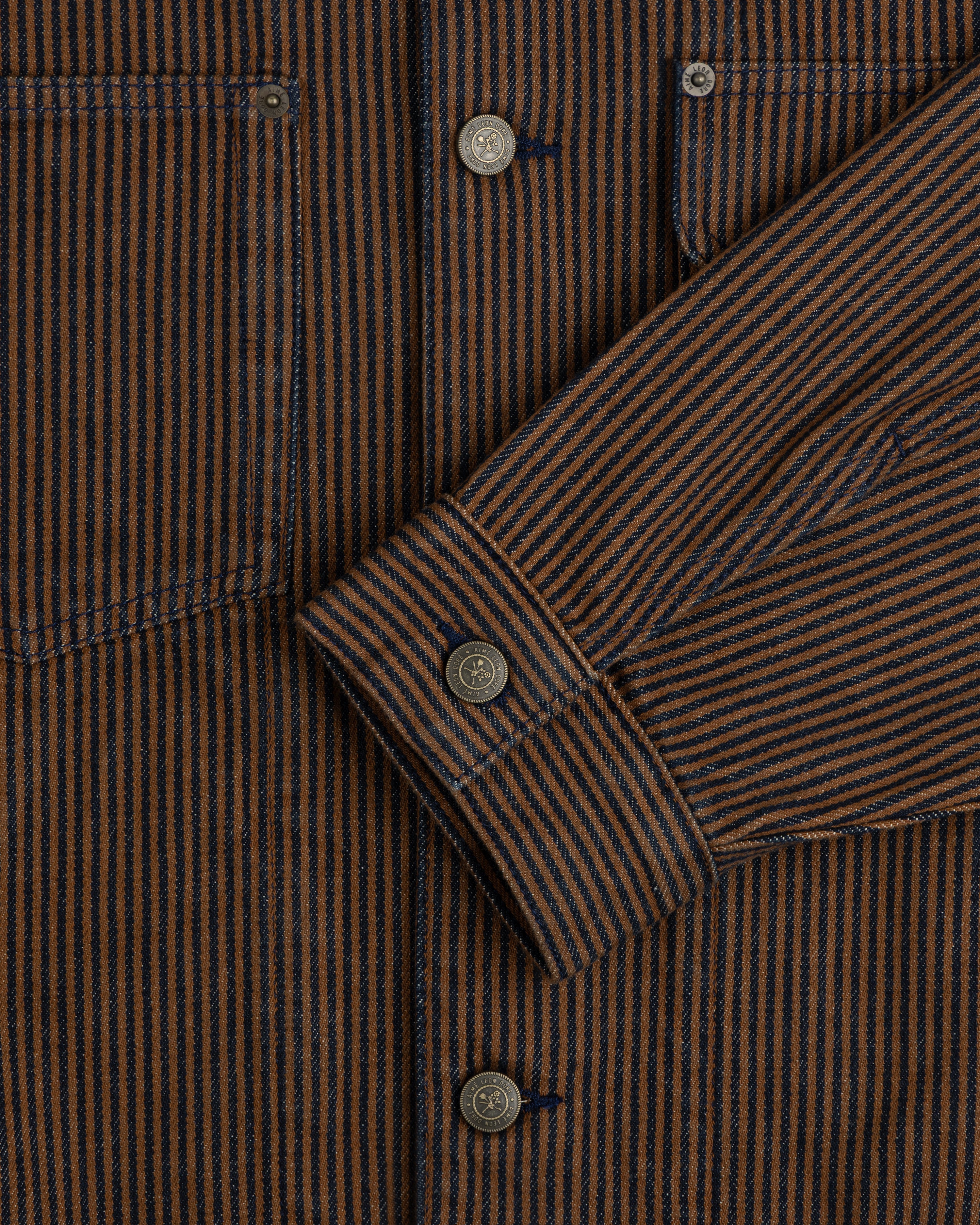 Close-up of the Hickory Stripe Denim Trucker Jacket with brown/navy stripes, metal buttons, and detailed pockets/sleeves.