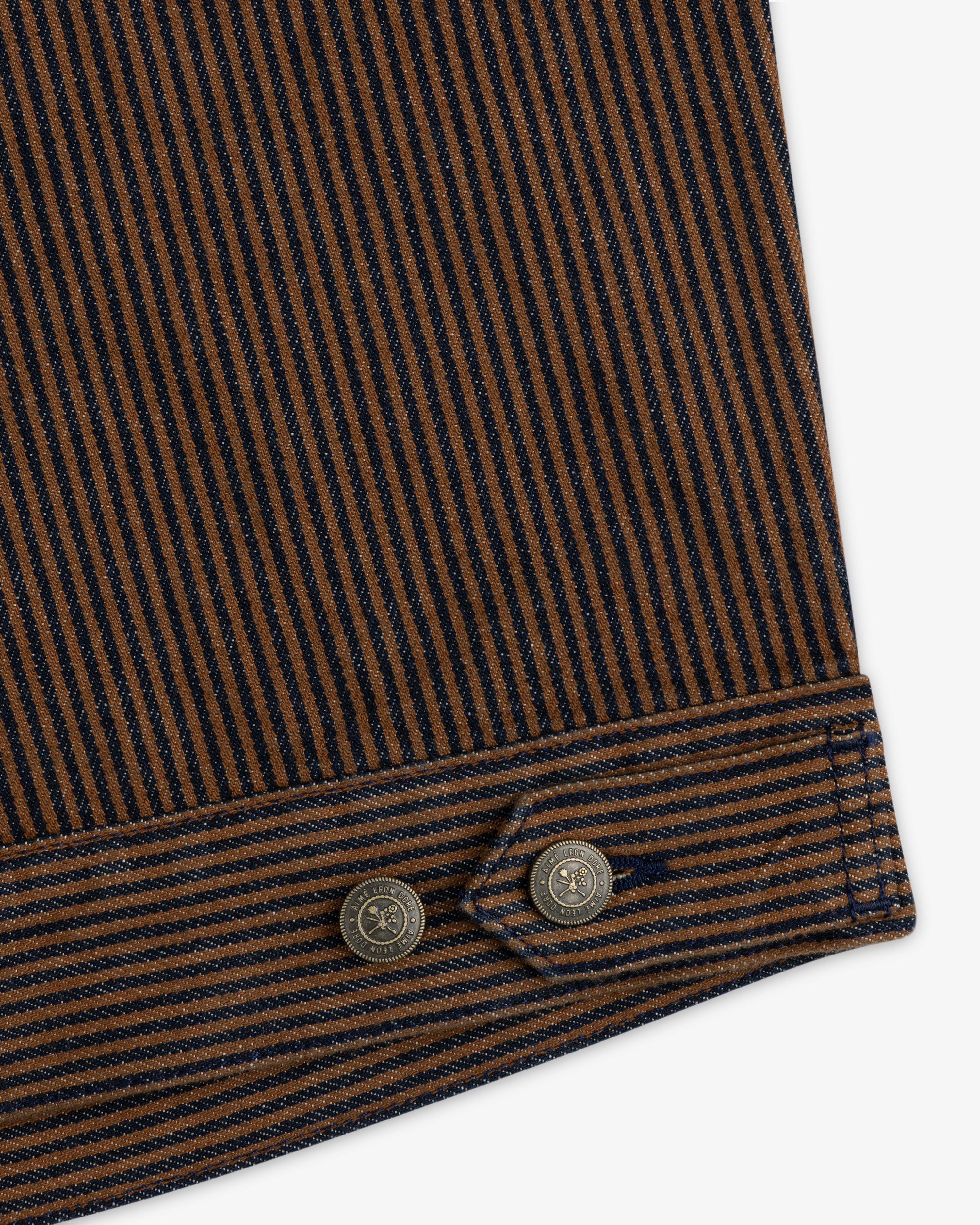 Hickory Stripe Denim Trucker Jacket with brown-navy stripes, visible stitching, and two metal buttons on cuffed edges.