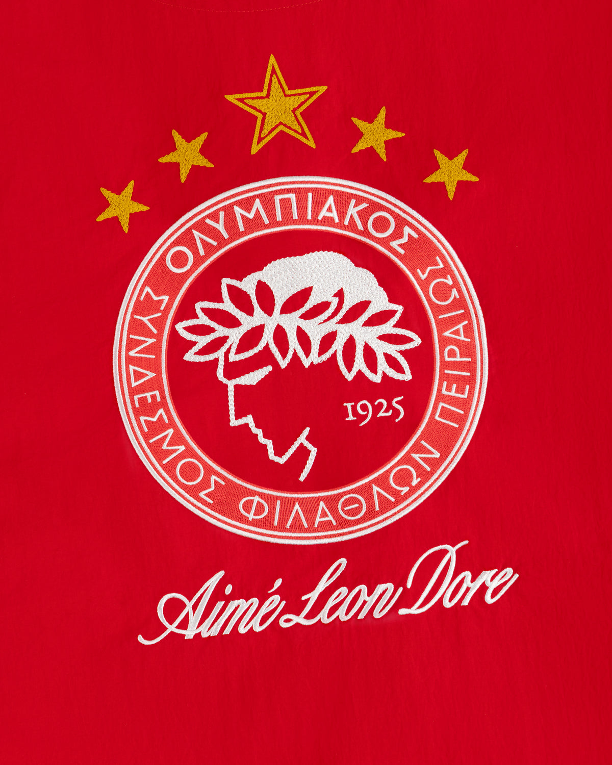 An embroidered crest on red fabric from the ALD / Olympiacos F.C. Nylon Quarter Zip Pullover with a laurel profile and stars.
