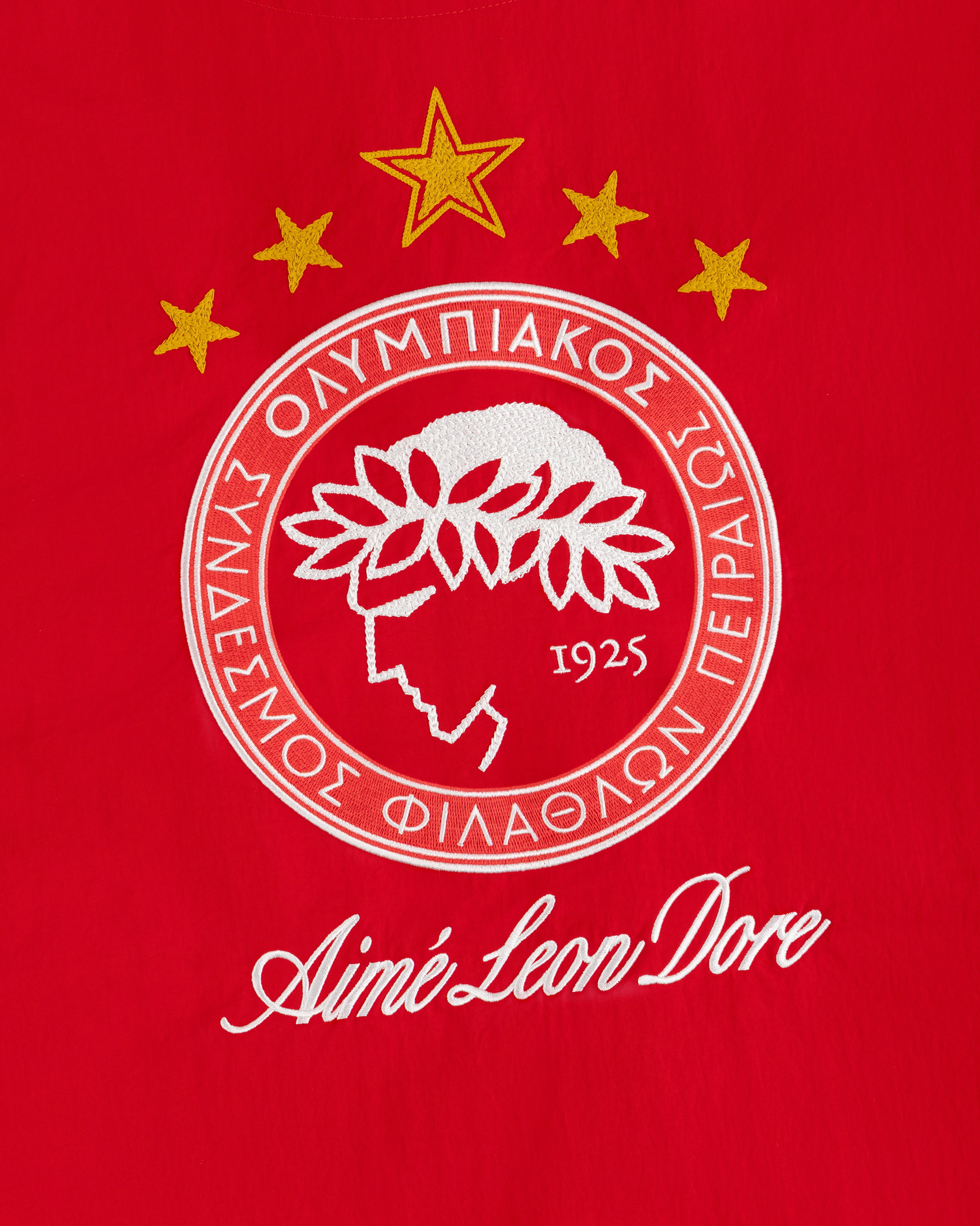 An embroidered crest on red fabric from the ALD / Olympiacos F.C. Nylon Quarter Zip Pullover with a laurel profile and stars.