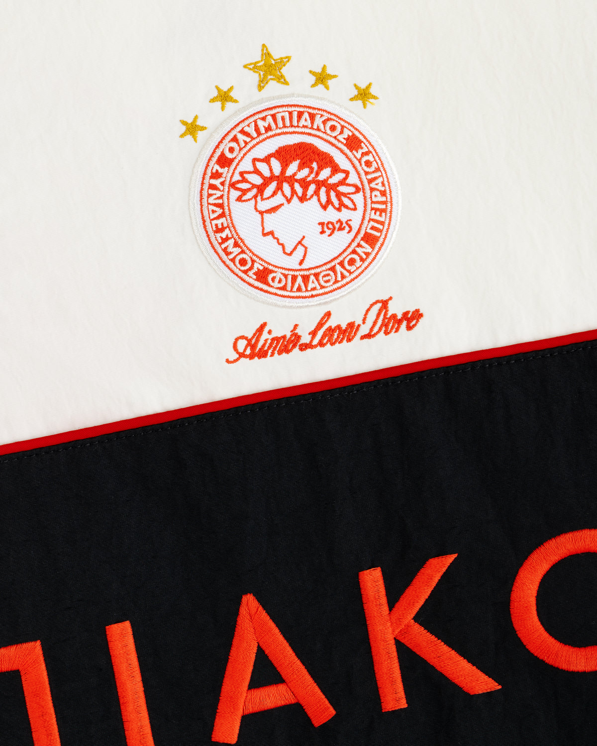 ALD / Olympiacos F.C. Nylon Quarter Zip Pullover in white with an embroidered logo and red lettering on a black panel.