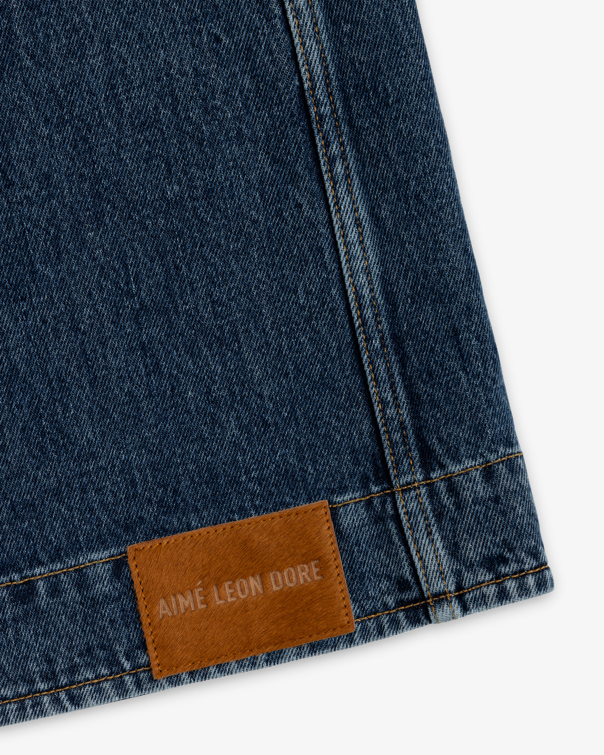 Denim Chore Coat in dark blue denim with gold stitching and a brown leather patch embossed with Aimé Leon Dore.