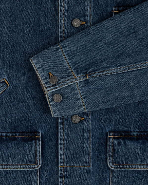 Close-up of a blue Denim Chore Coat featuring gold stitching, buttoned cuffs, and large patch pockets.