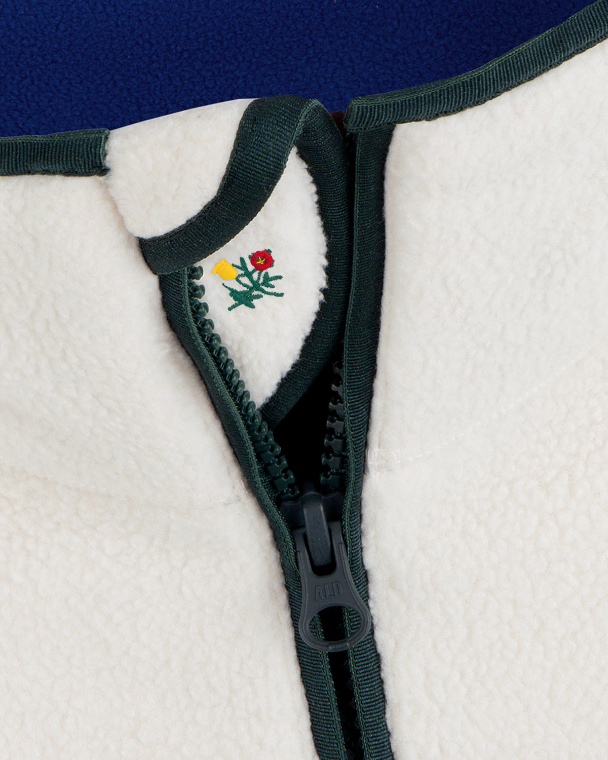 Cream-colored Script Fleece Half Zip Pullover with dark green trim and small floral embroidery near the collar.