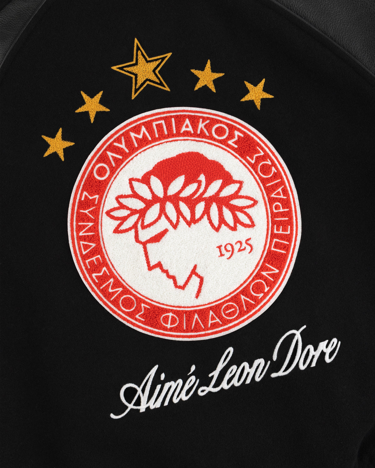 Embroidered red and white sports emblem above the brand name on a black ALD / Olympiacos F.C. Team Leather Jacket.