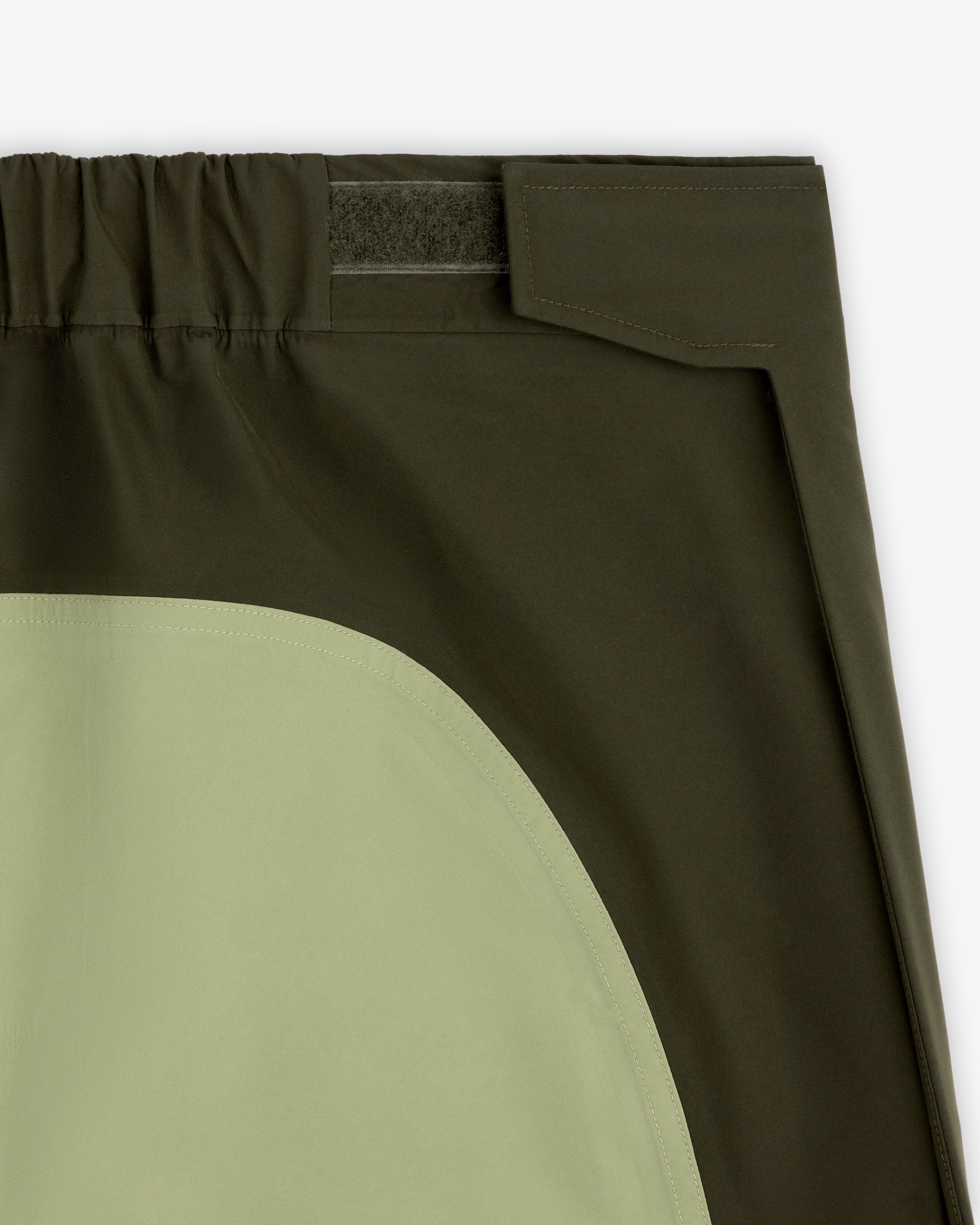 Close-up of ALD / The North Face GORE-TEX Pant: dark green, elastic waistband, Velcro closure, light green pocket.