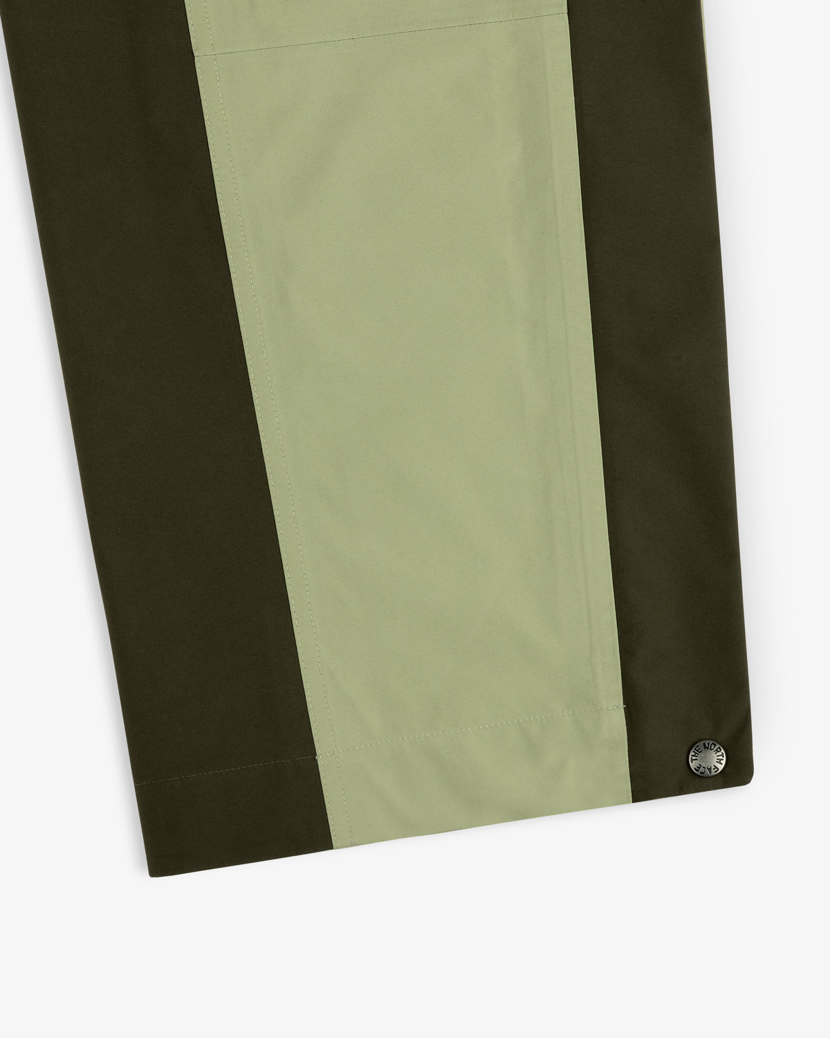 Close-up of ALD/The North Face GORE-TEX Pant in light green and dark olive with a round metal button at the edge.