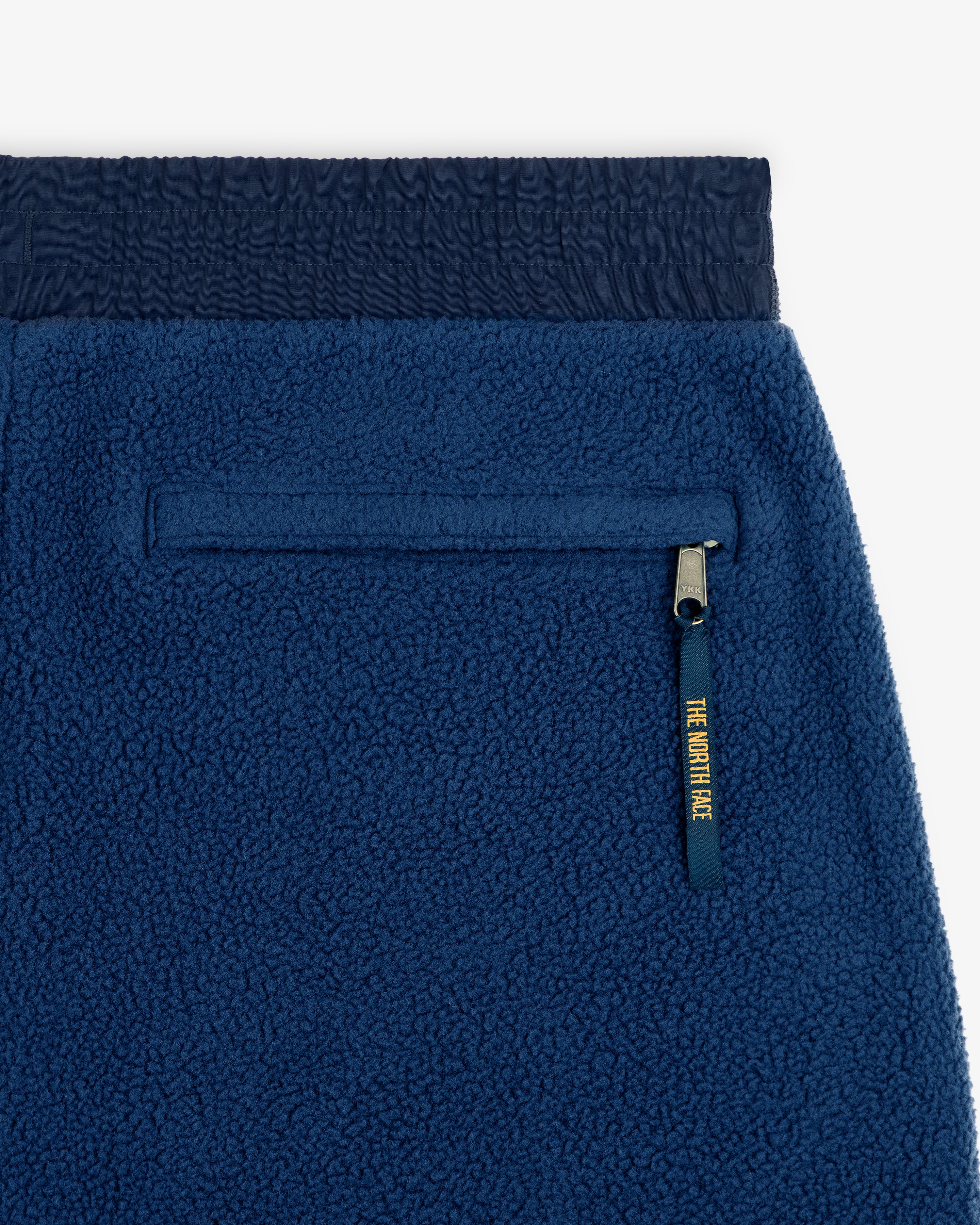 Close-up of ALD / The North Face Denali Fleece Pant: blue fleece, zip pocket with yellow pull tab, elastic waistband.
