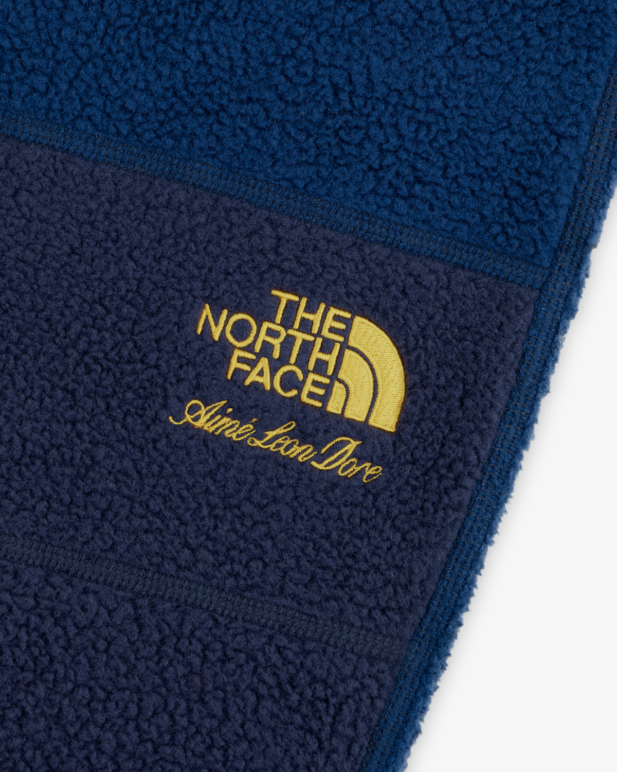 Close-up of blue ALD / The North Face Denali Fleece Pant with yellow embroidered logos.