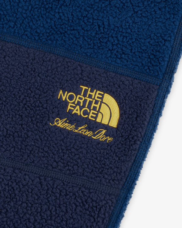 Close-up of blue ALD / The North Face Denali Fleece Pant with yellow embroidered logos.