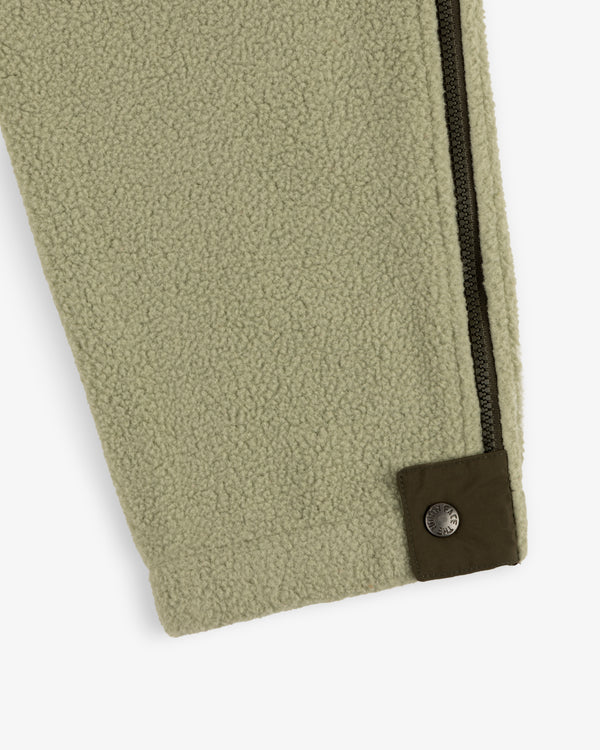 Detail of the ALD/The North Face Denali Fleece Pant in light green, featuring a dark zipper and brown snap button cuff.