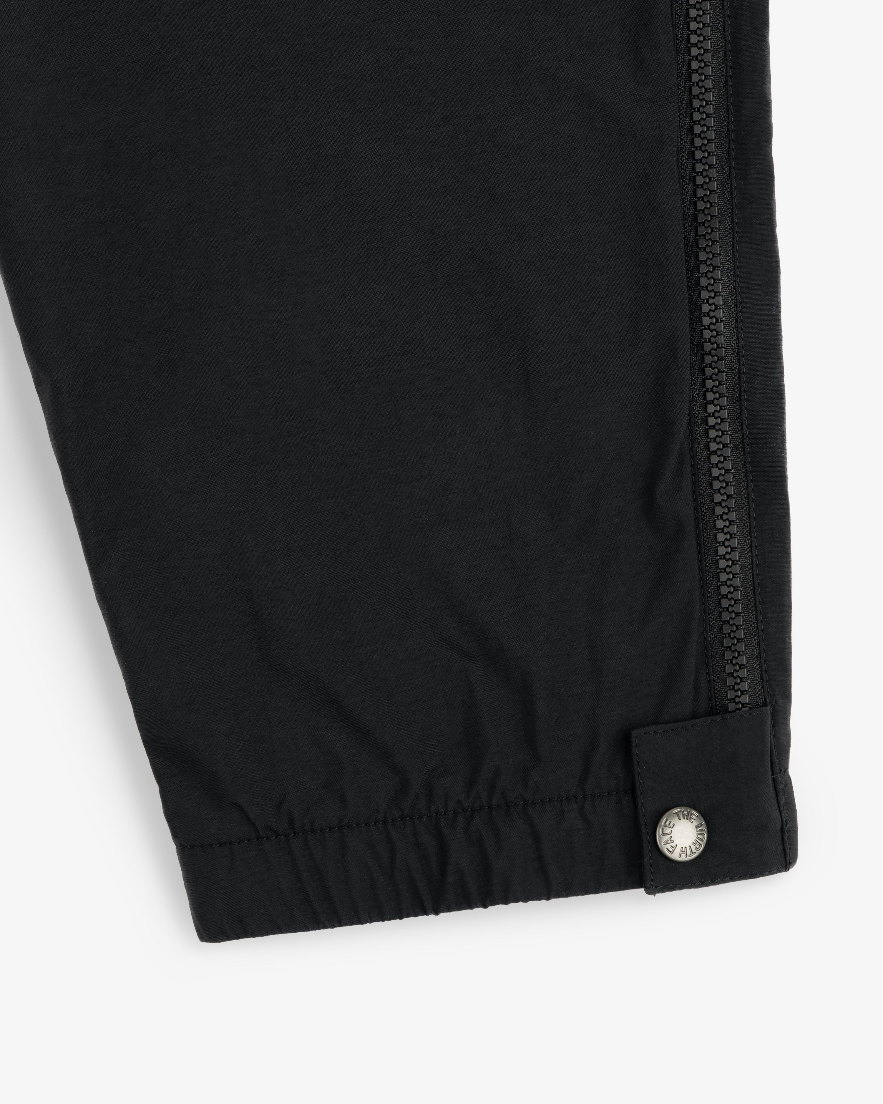 Close-up of ALD / The North Face Nylon Denali Pant showing a black pant leg with zipper and silver snap at the cuff.