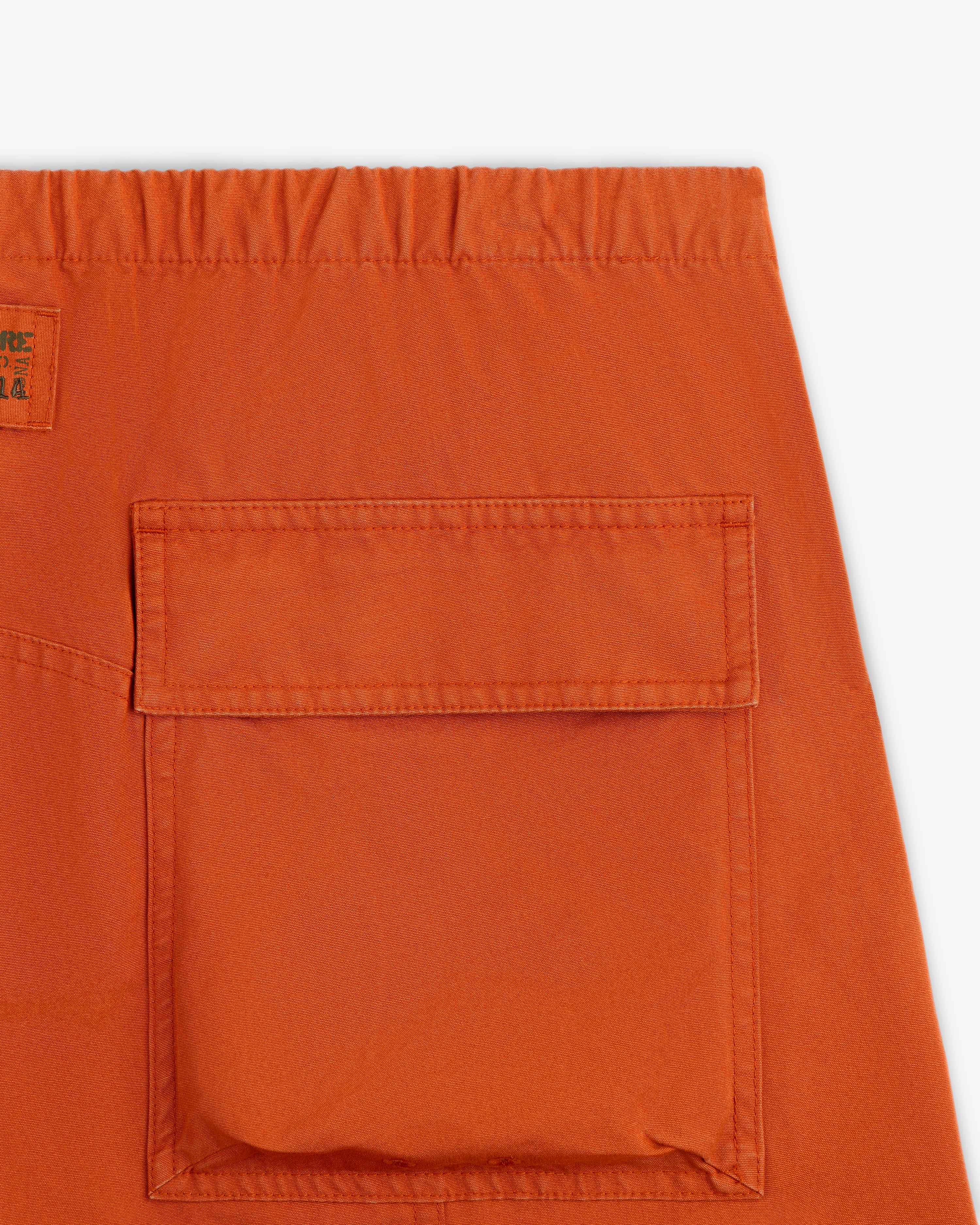 Close-up of an orange Garment Washed Aviator Pant leg featuring a large patch pocket and an elastic waistband.