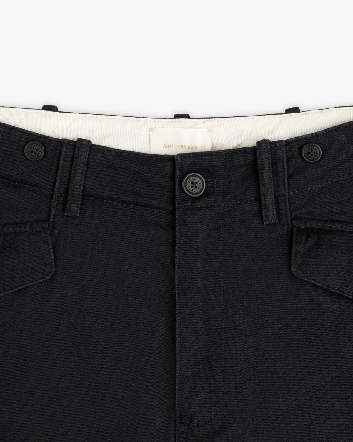 Close-up of the Fatigue Pant’s black waistband with two buttons, belt loops, and flap pockets on white background.
