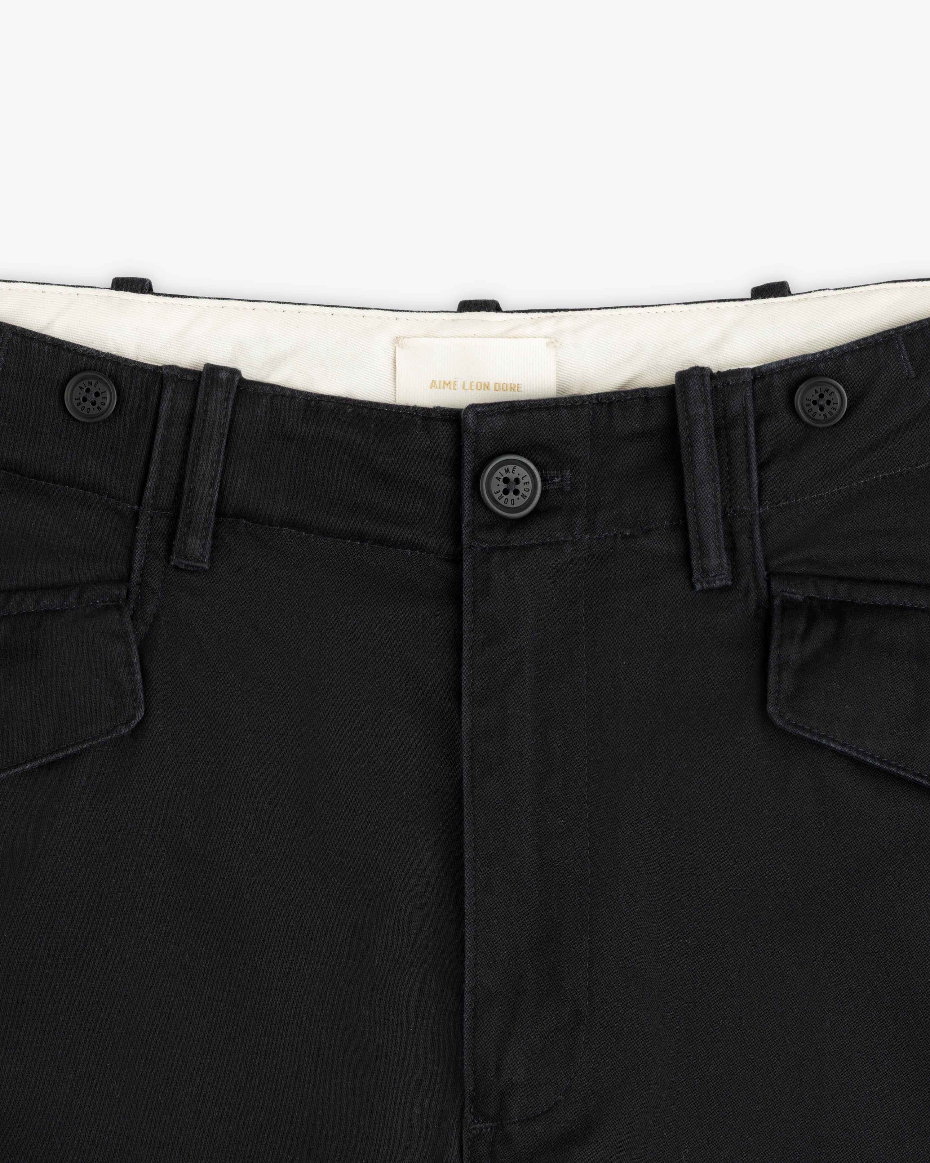 Close-up of the Fatigue Pant’s black waistband with two buttons, belt loops, and flap pockets on white background.