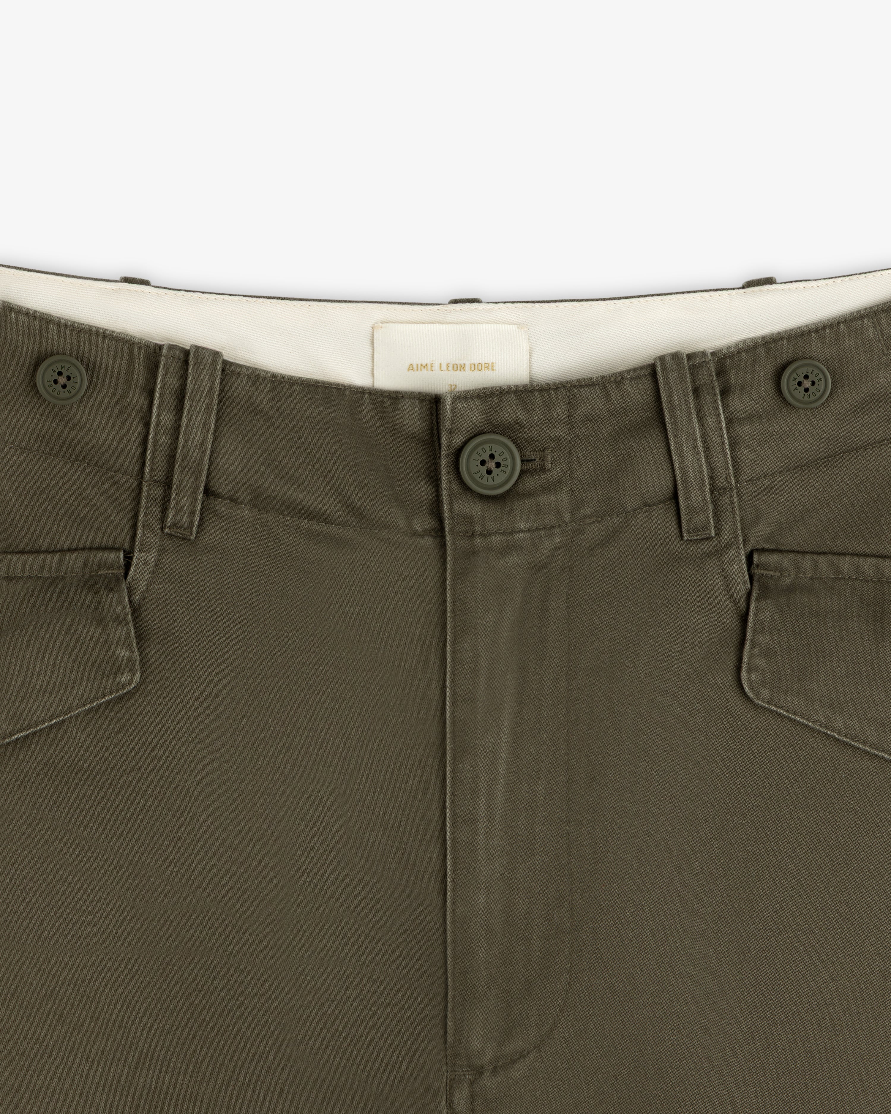 Close-up of Fatigue Pant in olive green, featuring button closure, front pockets, and a white waistband label.