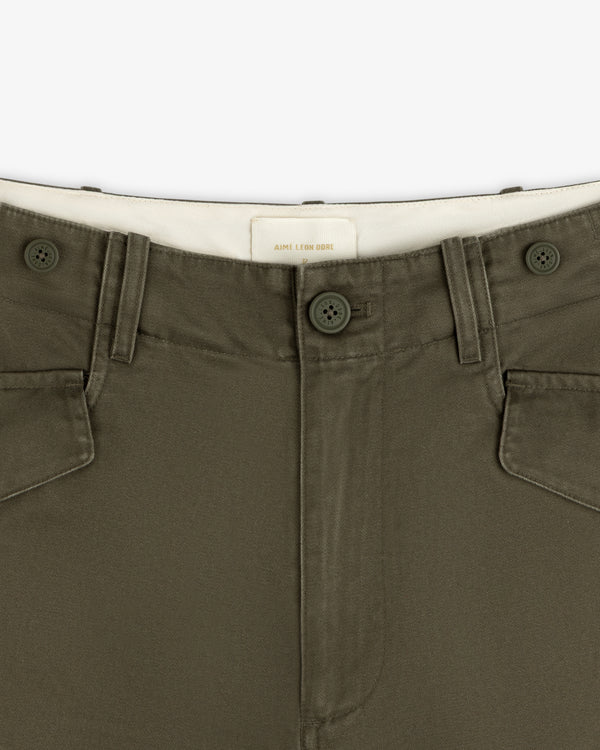 Close-up of Fatigue Pant in olive green, featuring button closure, front pockets, and a white waistband label.
