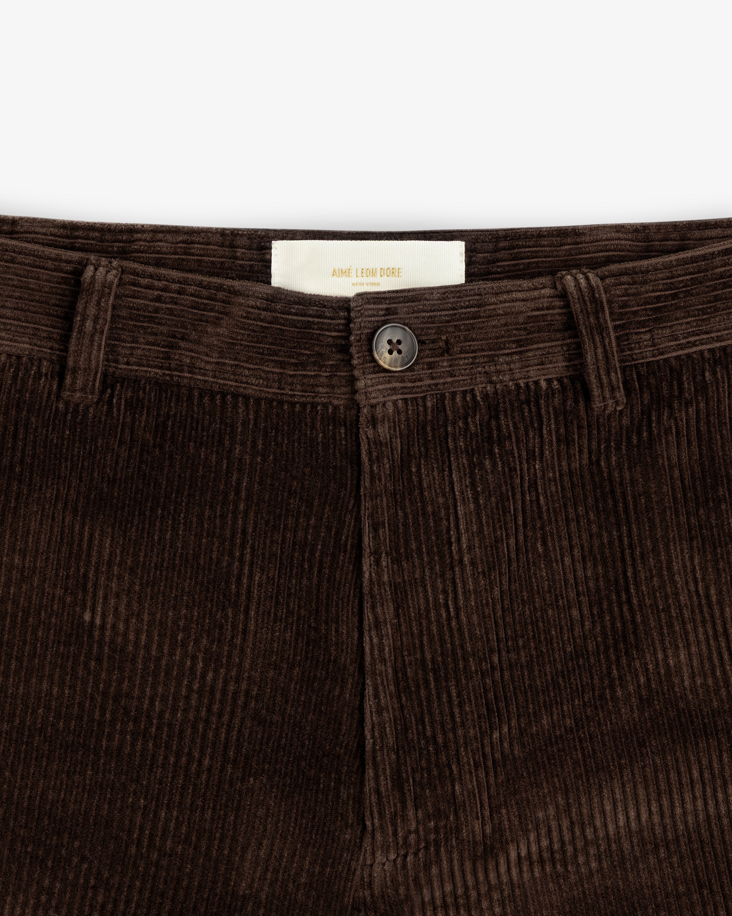 Close-up of brown Corduroy Trouser featuring a button closure and a brand label at the waistband.