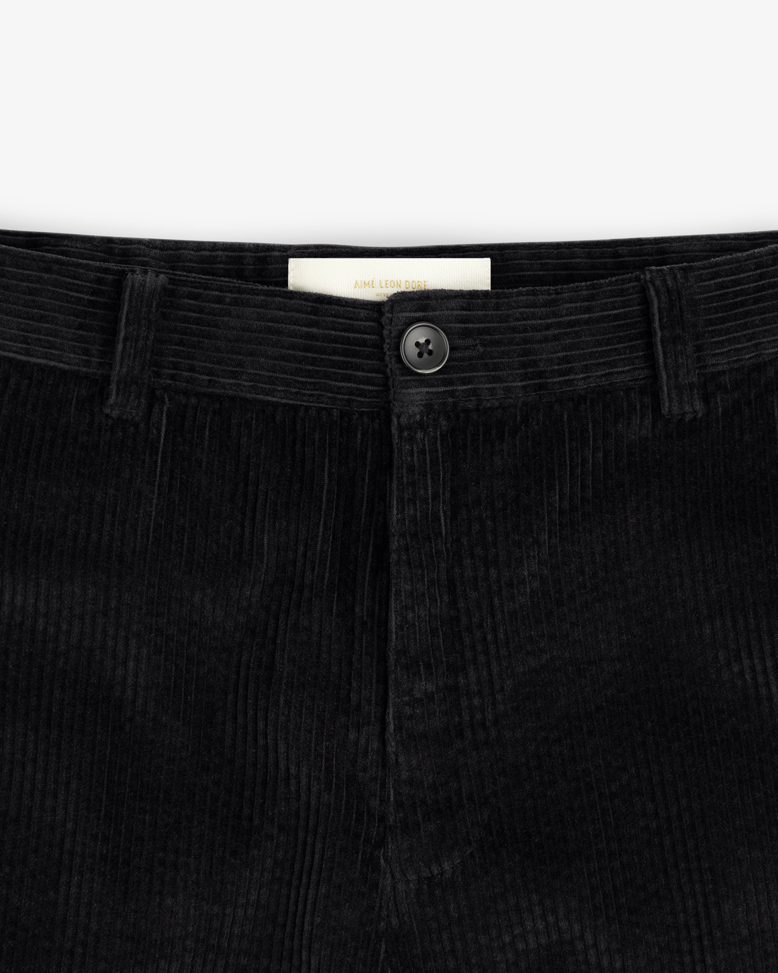Close-up of the waistband of black Corduroy Trouser corduroy trousers, featuring a center button and a brand label.