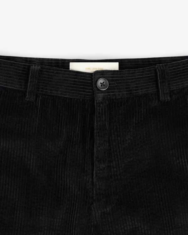 Close-up of the waistband of black Corduroy Trouser corduroy trousers, featuring a center button and a brand label.