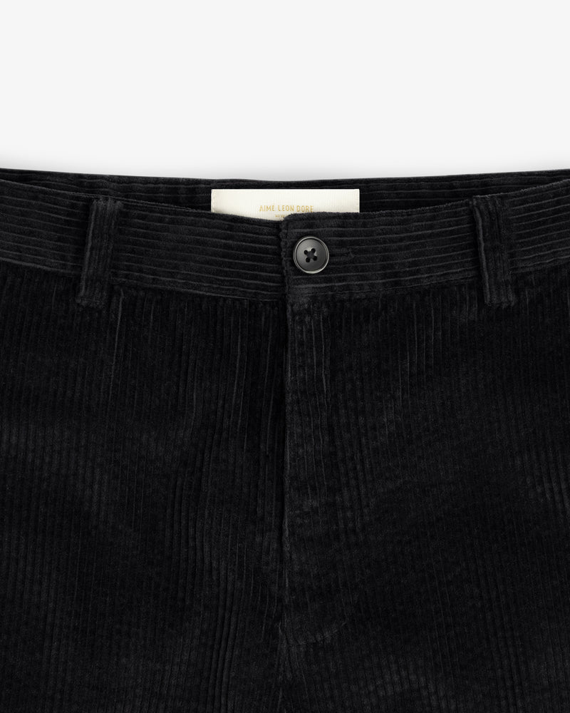 Close-up of the waistband of black Corduroy Trouser corduroy trousers, featuring a center button and a brand label.