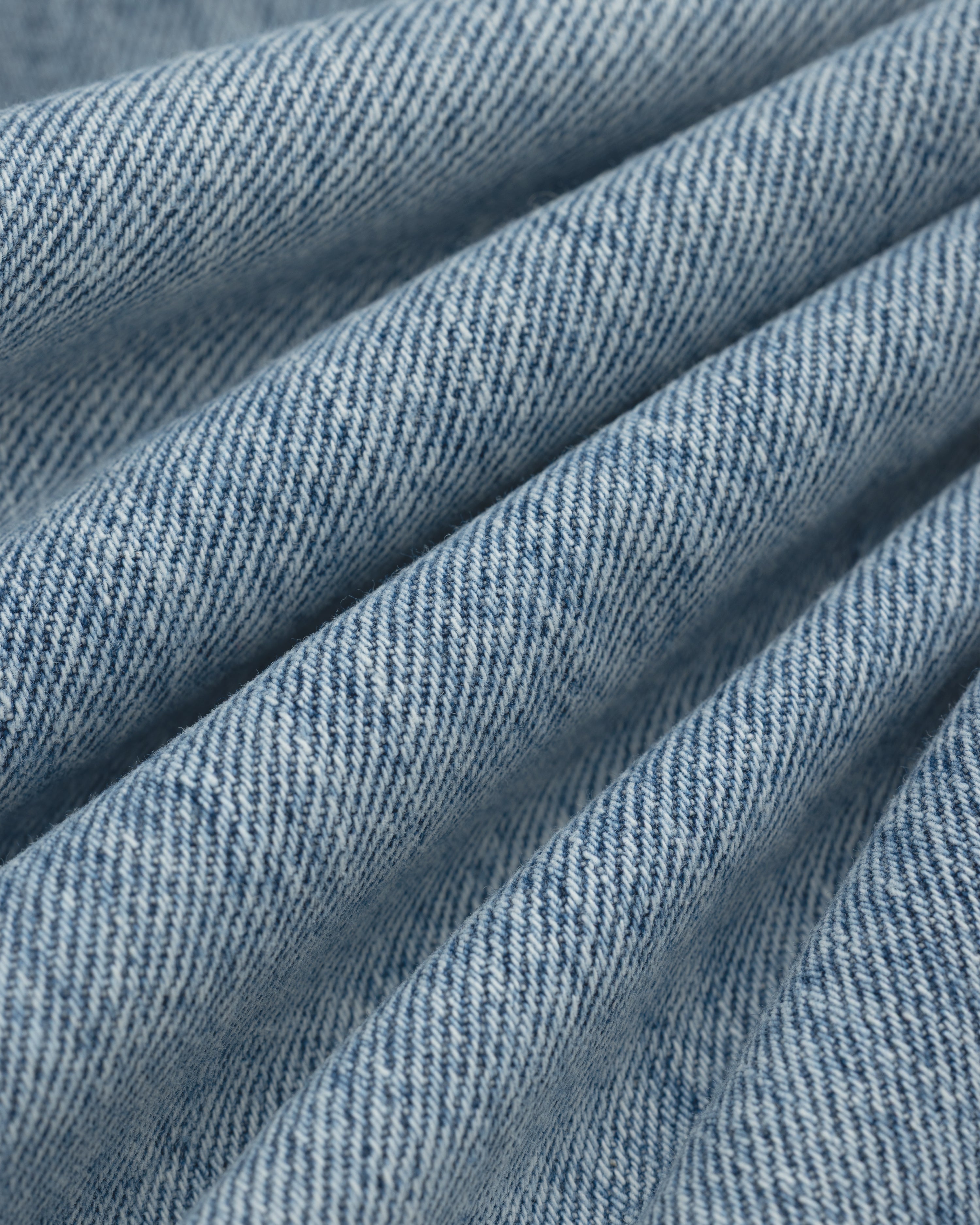 Close-up of light blue ALD Relaxed Fit Denim fabric with diagonal folds.
