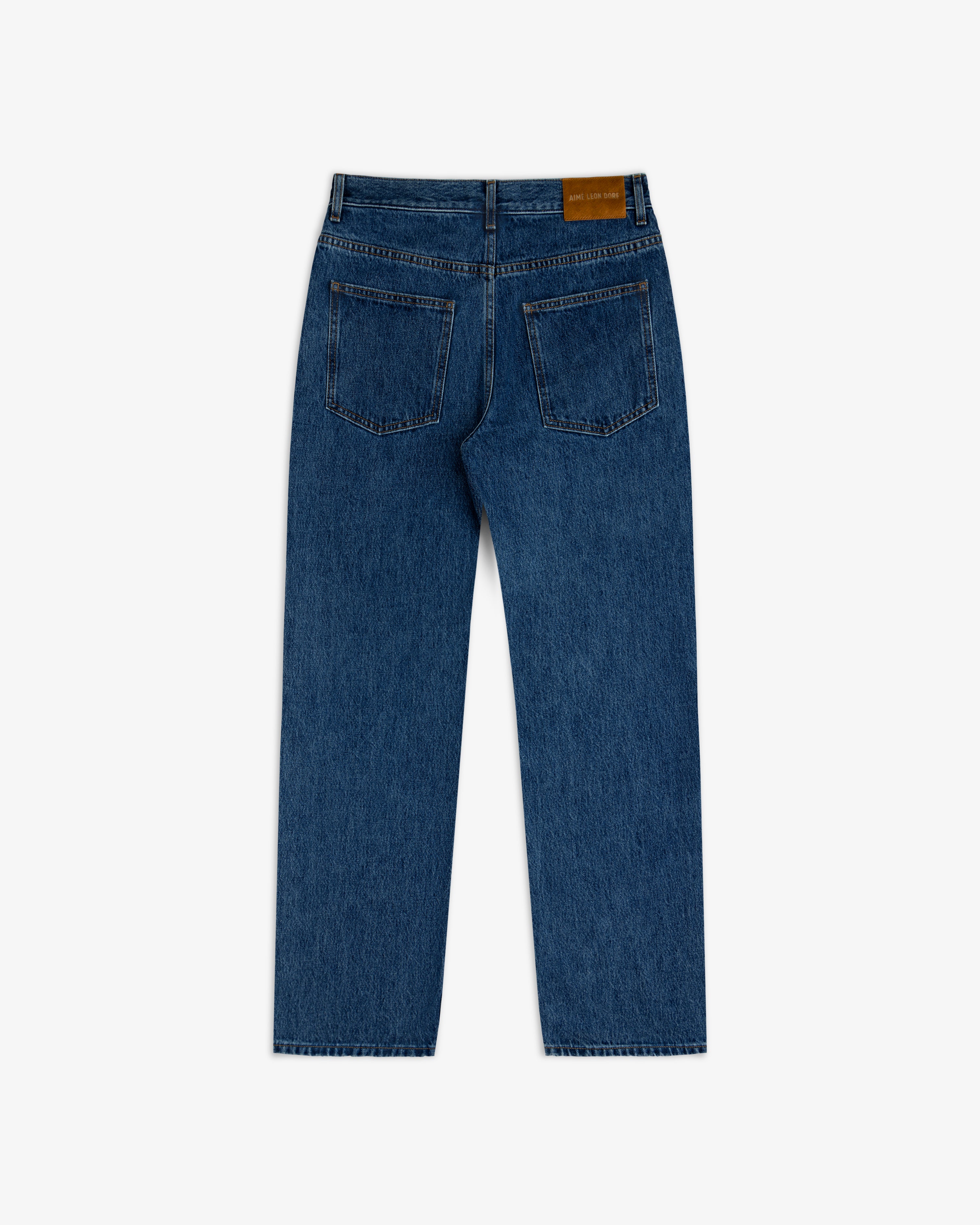 Back view of ALD Relaxed Fit Denim in dark wash blue, featuring two back pockets and a leather logo patch on the waistband.