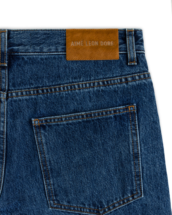 Back pocket of ALD Relaxed Fit Denim blue jeans with a tan leather patch featuring embossed text.