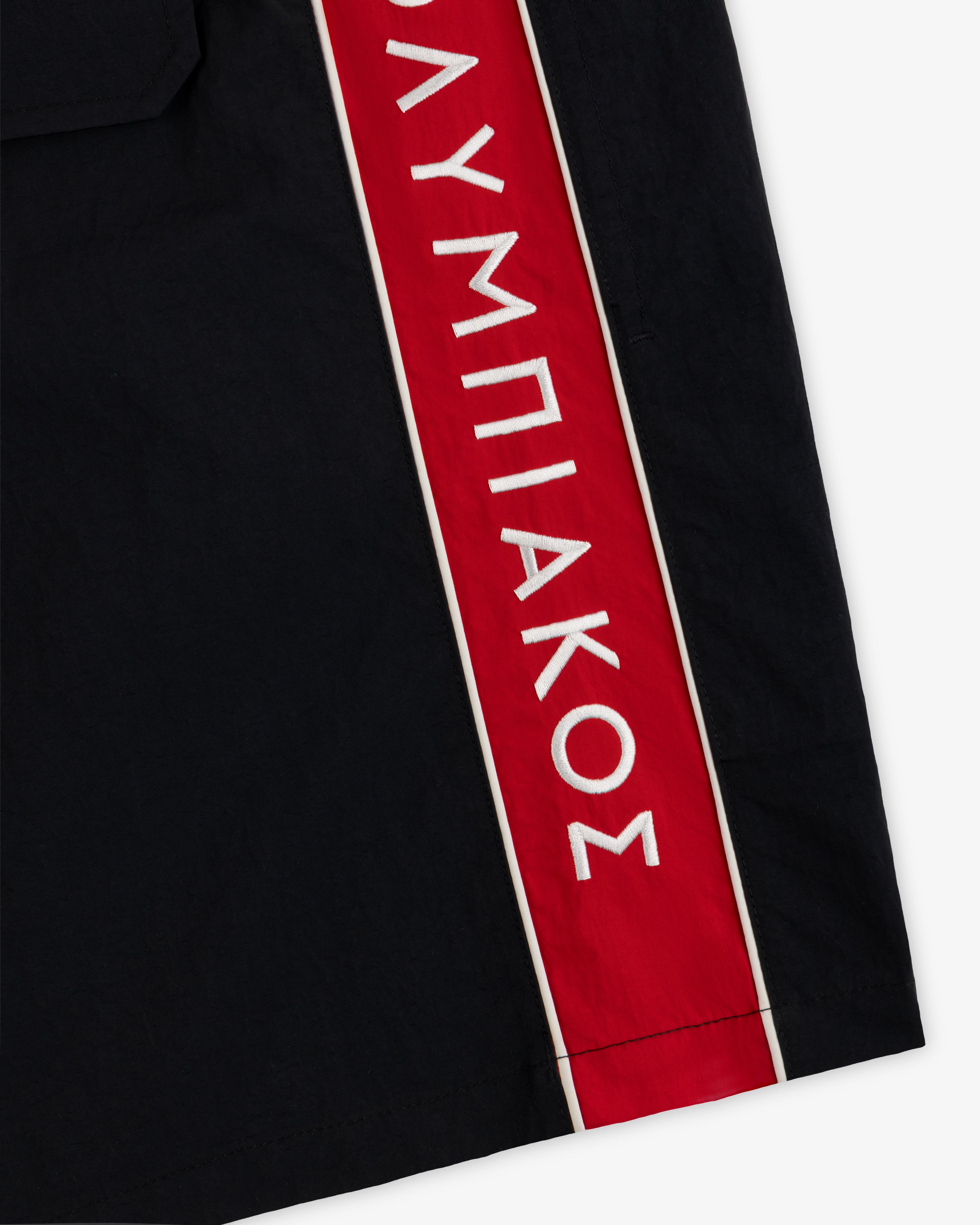 ALD / Olympiacos F.C. Nylon Training Short: black athletic shorts with a red vertical side stripe featuring white Greek text.