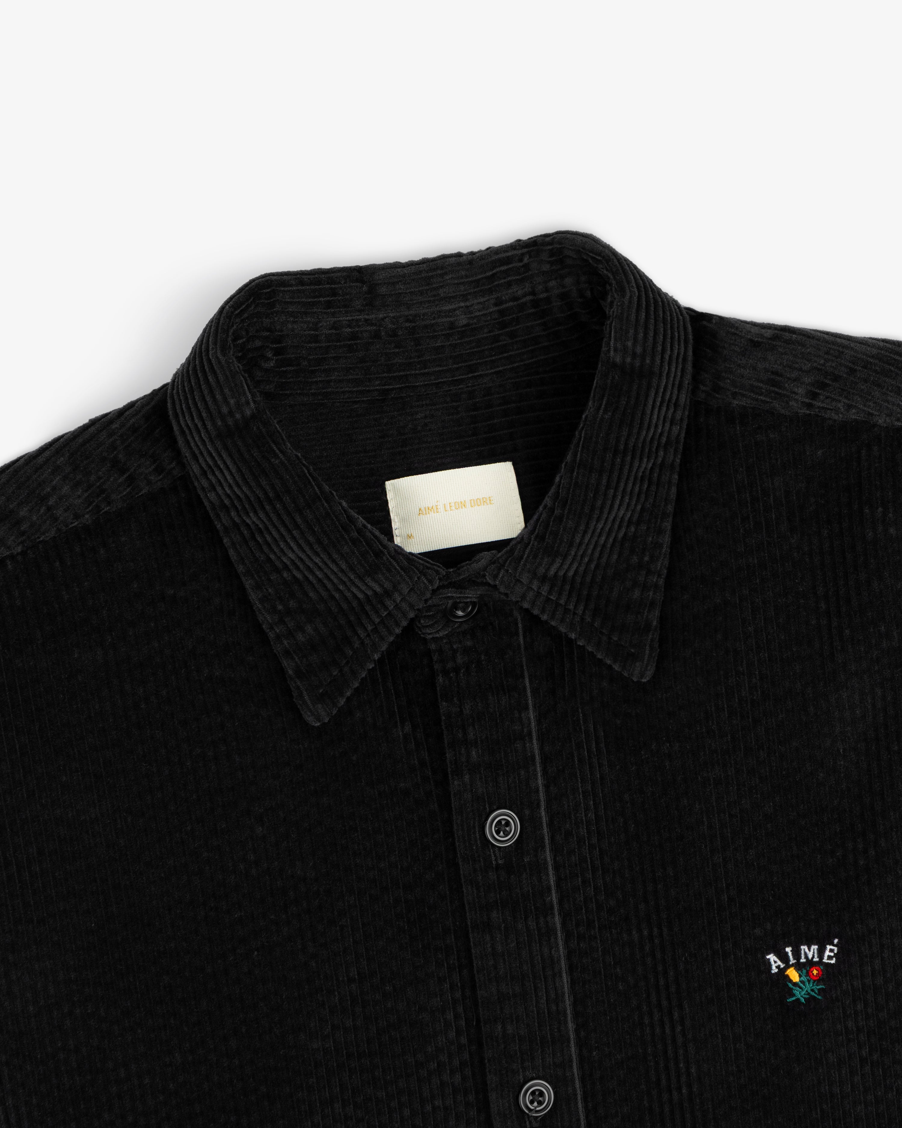 Corduroy Leon Overshirt in black corduroy with a button-down front and an embroidered flower logo on the chest.