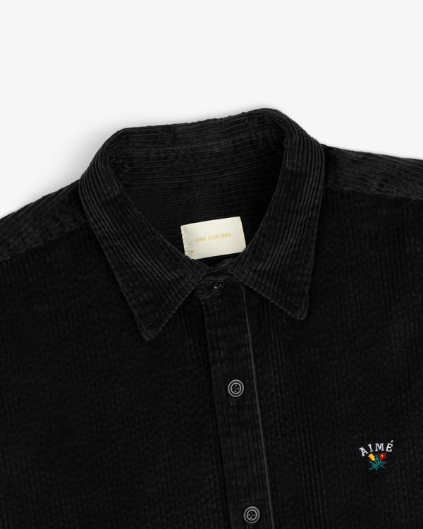 Corduroy Leon Overshirt in black corduroy with a button-down front and an embroidered flower logo on the chest.