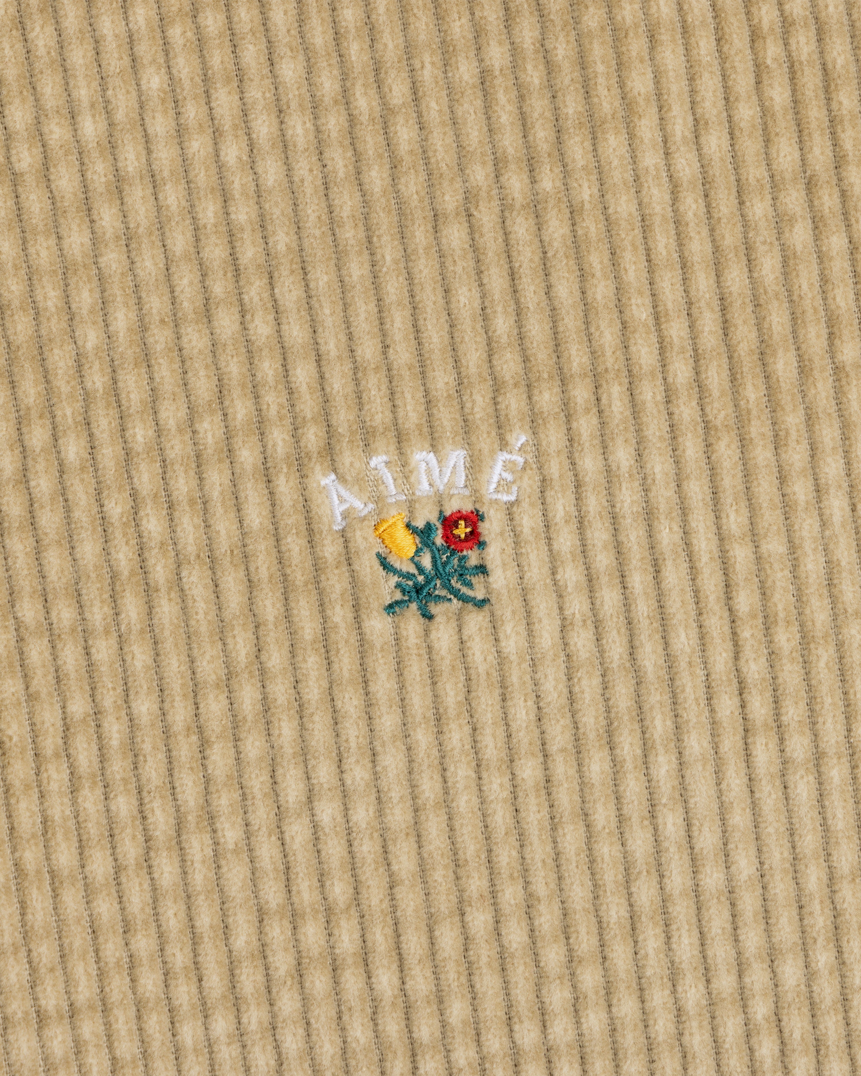 Tan Corduroy Leon Overshirt featuring an embroidered yellow and red flower with the text AIMÉ arched above it.
