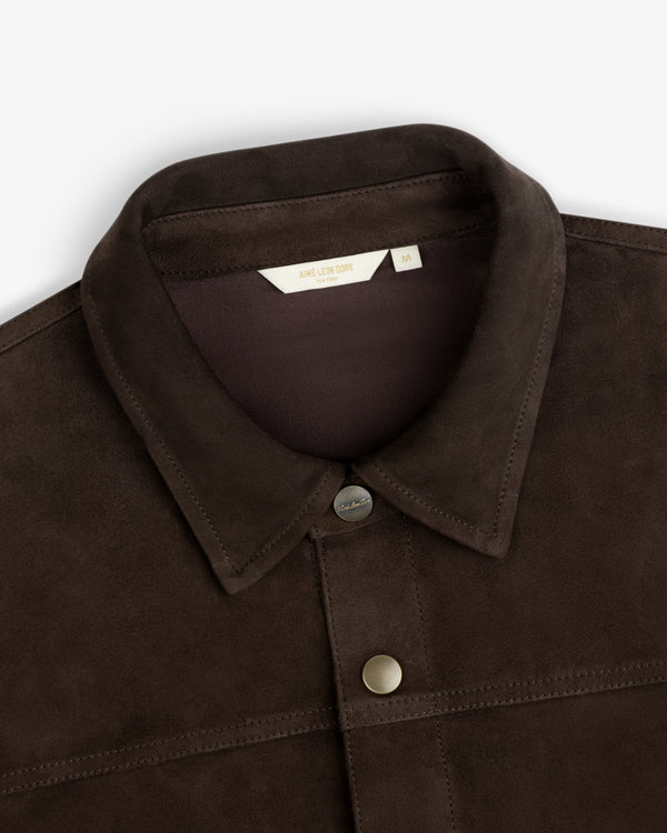 Close-up of a dark brown Suede Overshirt with a collar, buttons, and a brand label at the neckline.