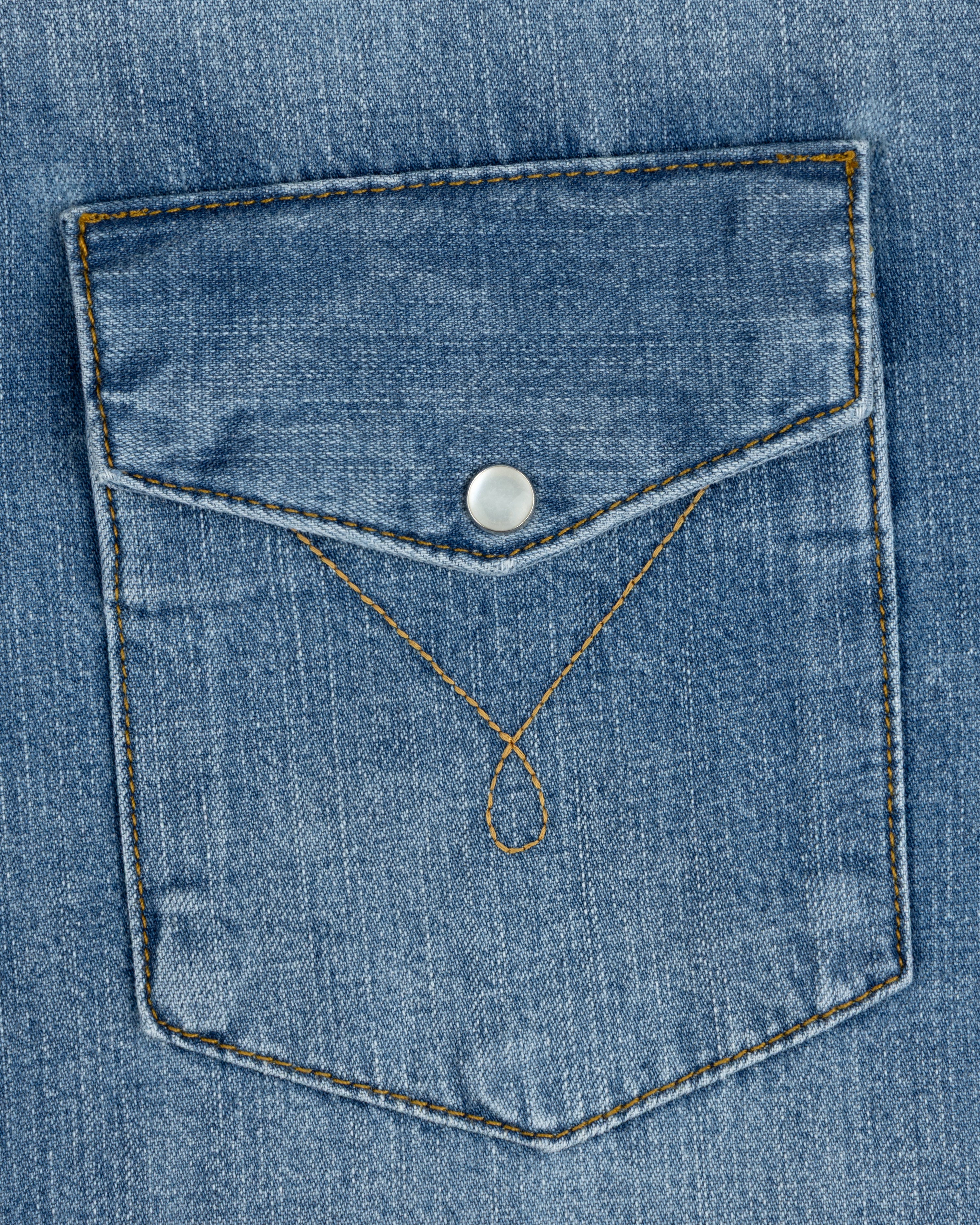 A Denim Western Shirt pocket with a pointed flap, silver snap button, and decorative gold stitching.