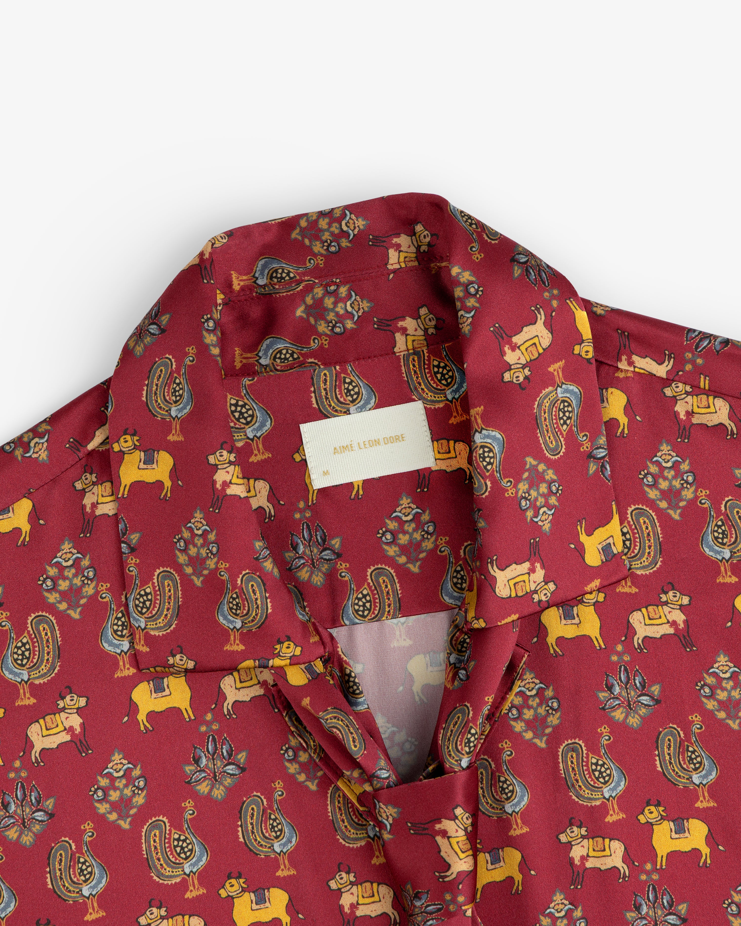 Archival Print Silk Tie Neck Blouse in burgundy with a stylized animal and floral print and a collared neckline.