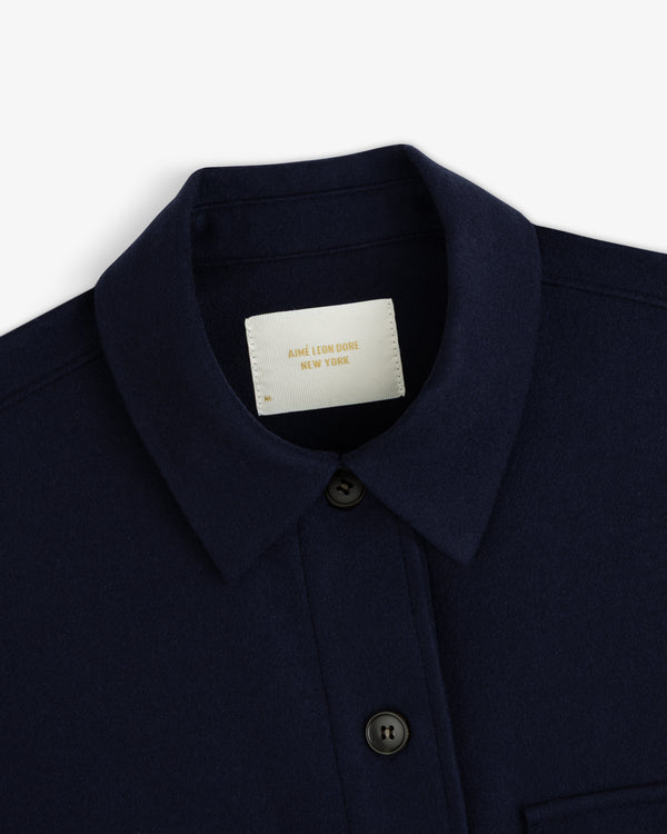 Close-up of a navy blue Mani Embroidered Wool jacket with a button-down front and a label at the collar.