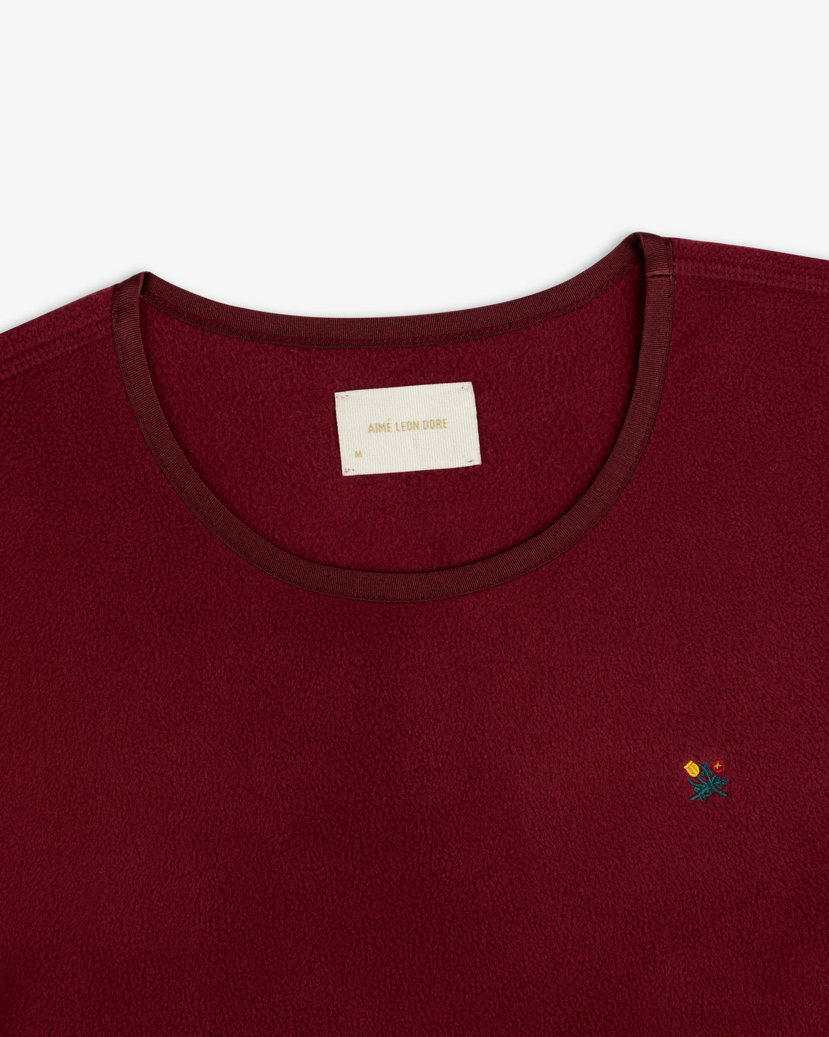 Maroon Crest Long-Sleeve Fleece Tee with a branded neck label and small floral embroidery on the chest.