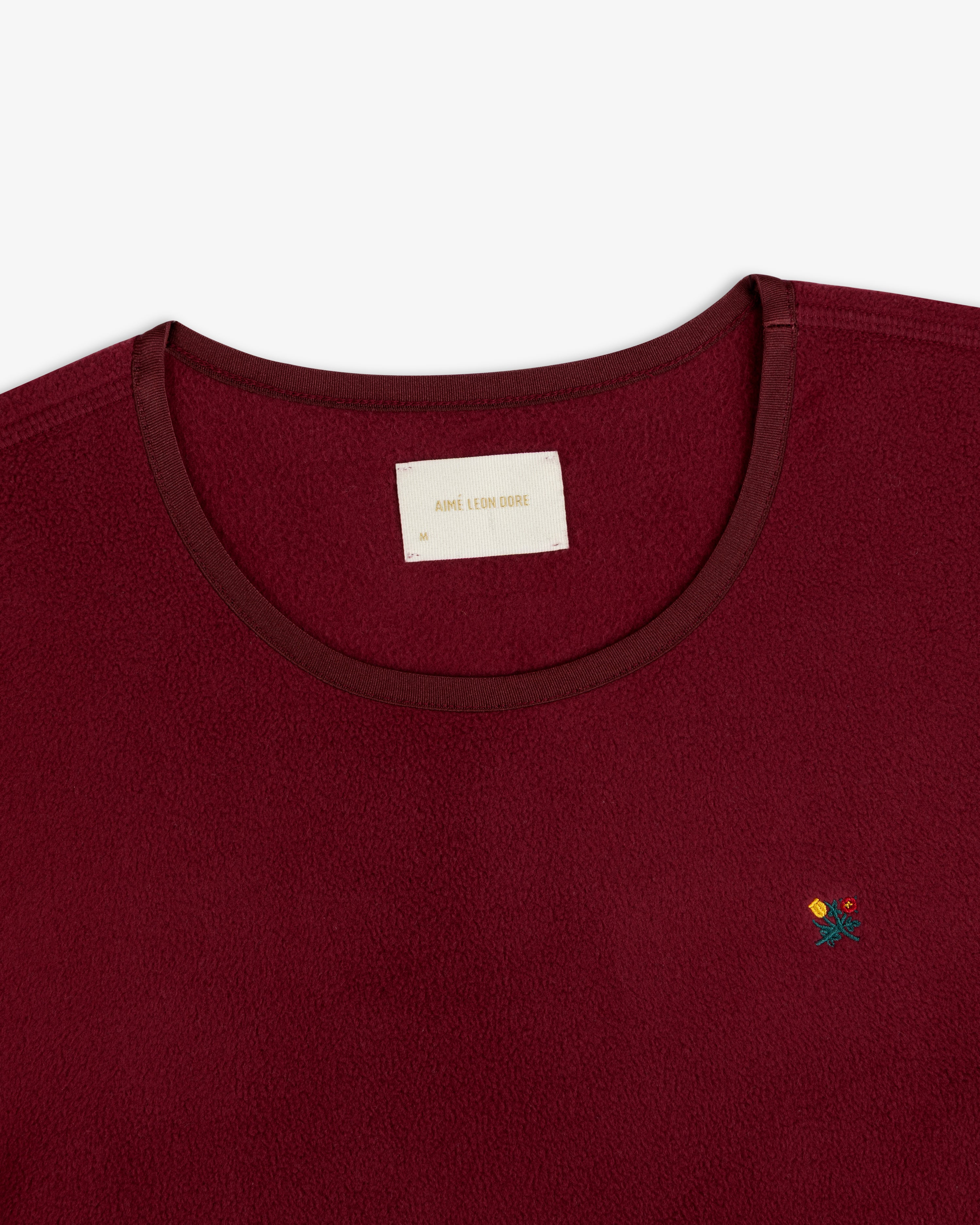 Maroon Crest Long-Sleeve Fleece Tee with a branded neck label and small floral embroidery on the chest.