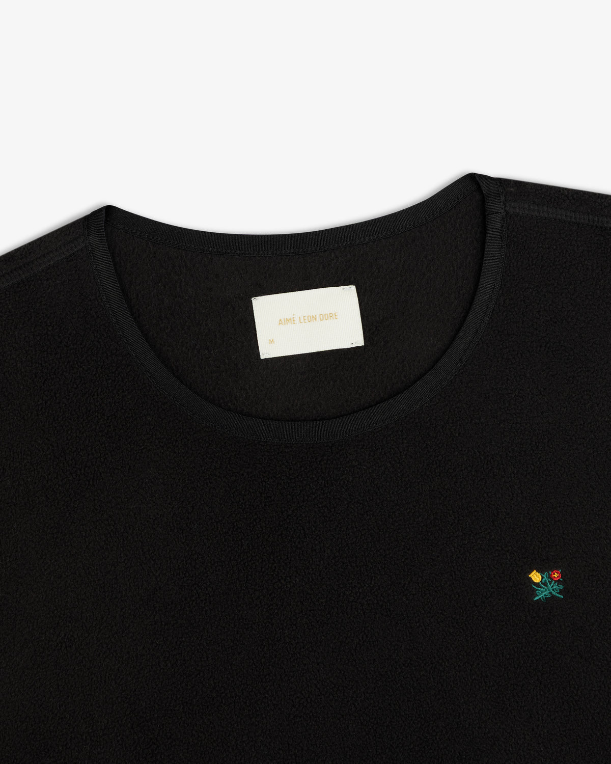 Black Crest Long-Sleeve Fleece Tee with small floral embroidery on the chest and an inner neckline brand label.
