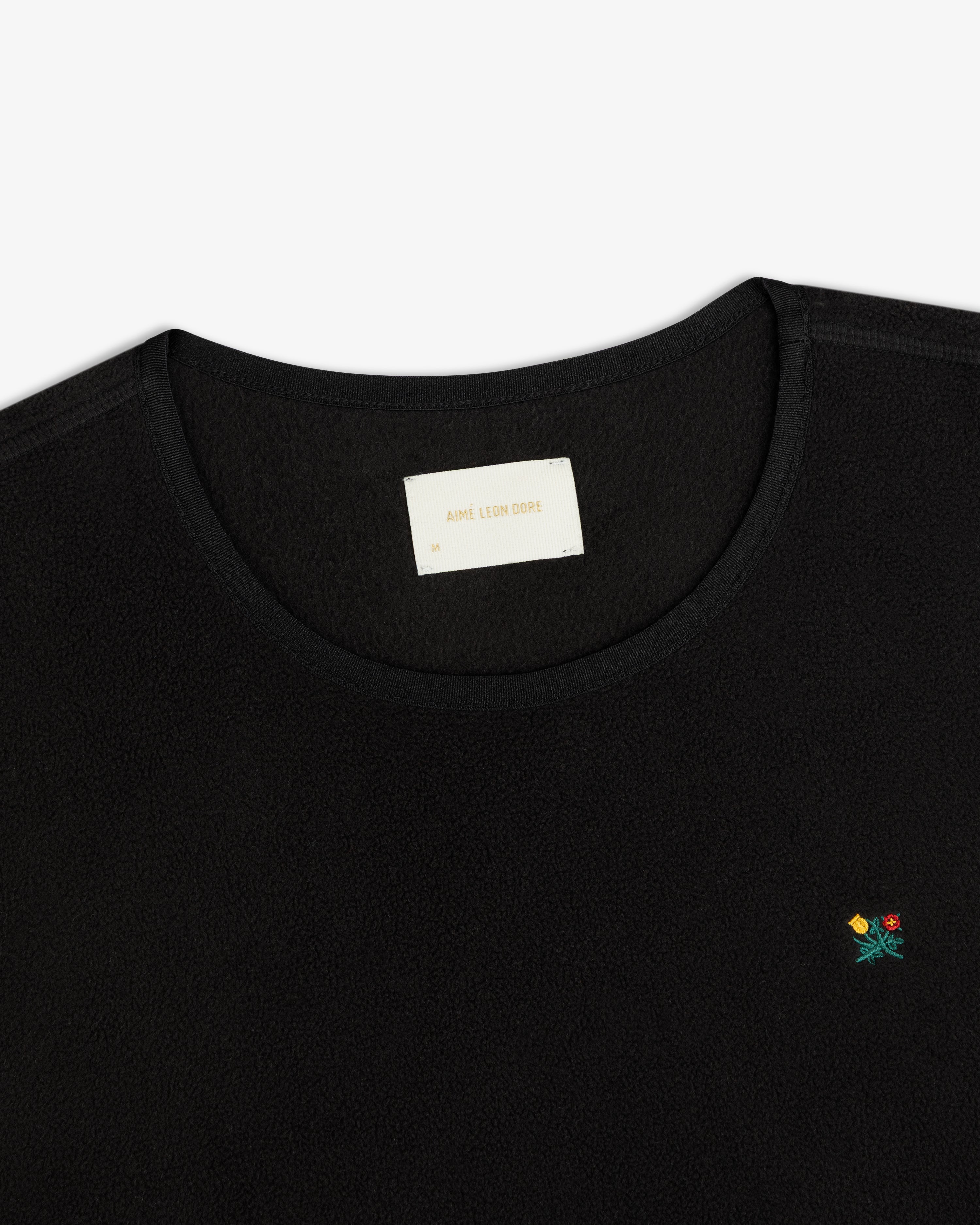 Black Crest Long-Sleeve Fleece Tee with small floral embroidery on the chest and an inner neckline brand label.