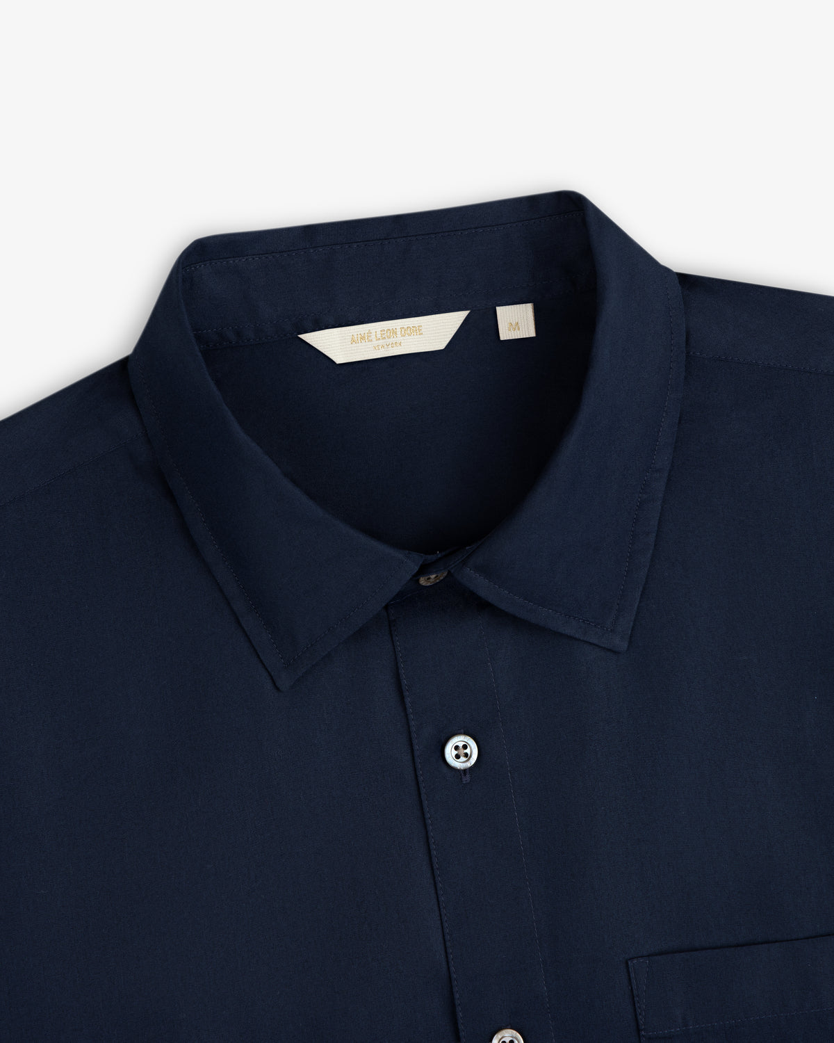 Close-up of a navy Poplin Casual Shirt with buttons and a beige Aimé Leon Dore size M label.
