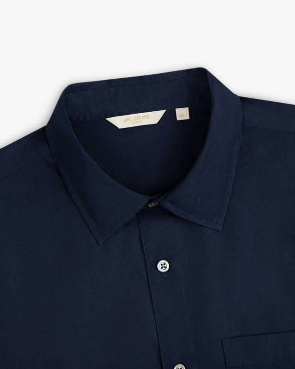 Close-up of a navy Poplin Casual Shirt with buttons and a beige Aimé Leon Dore size M label.