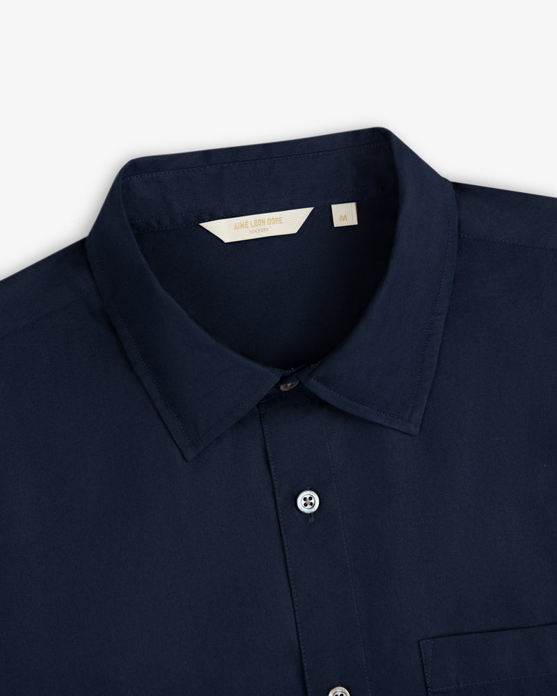 Close-up of a navy Poplin Casual Shirt with buttons and a beige Aimé Leon Dore size M label.