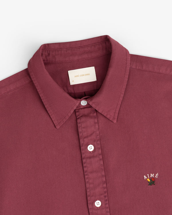 Garment Dyed Leon Overshirt: Maroon, collared, white buttons, AIMÉ rose logo on chest.